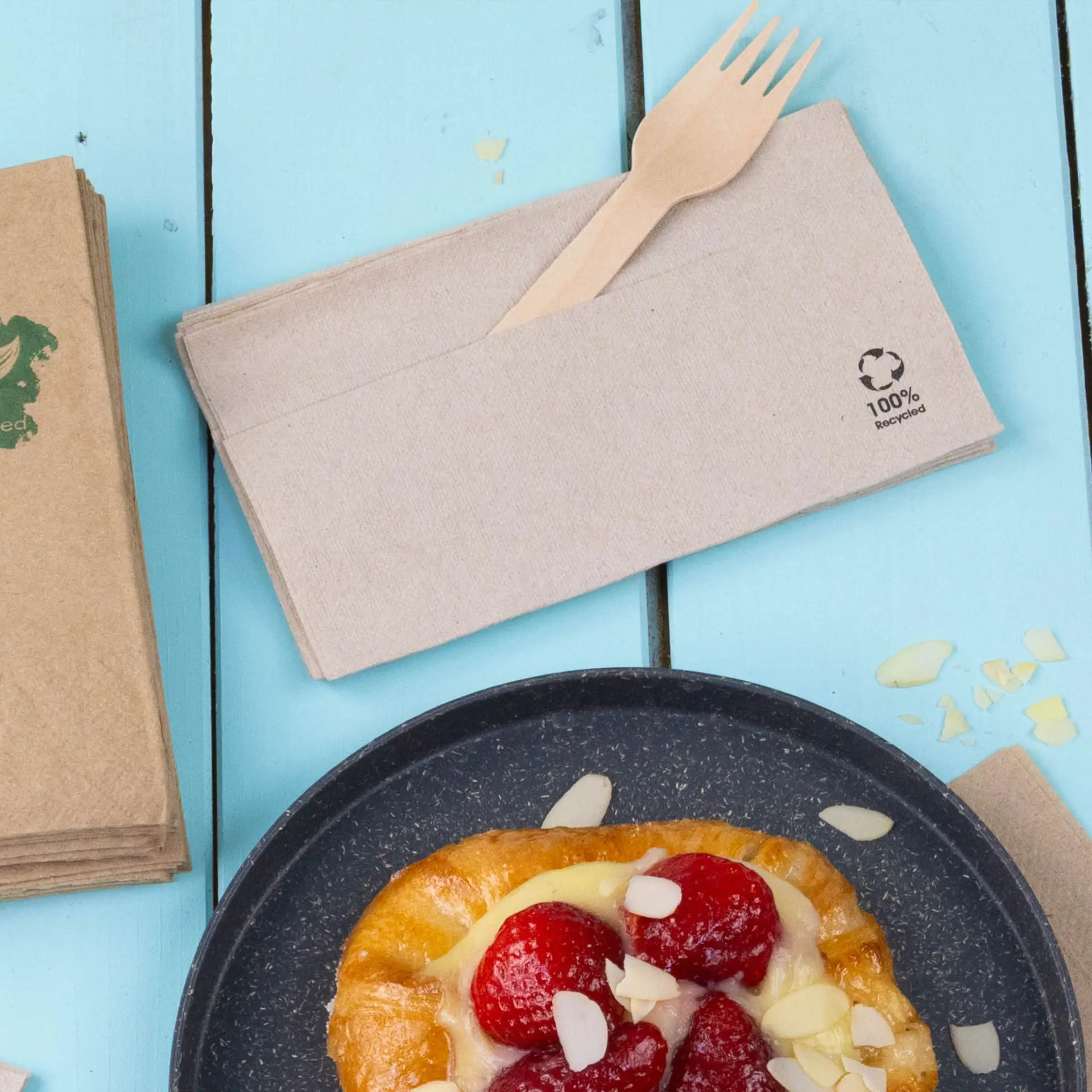 Papieren servetten van gerecycled papier, met een houten vork op een lichtblauwe houten ondergrond.