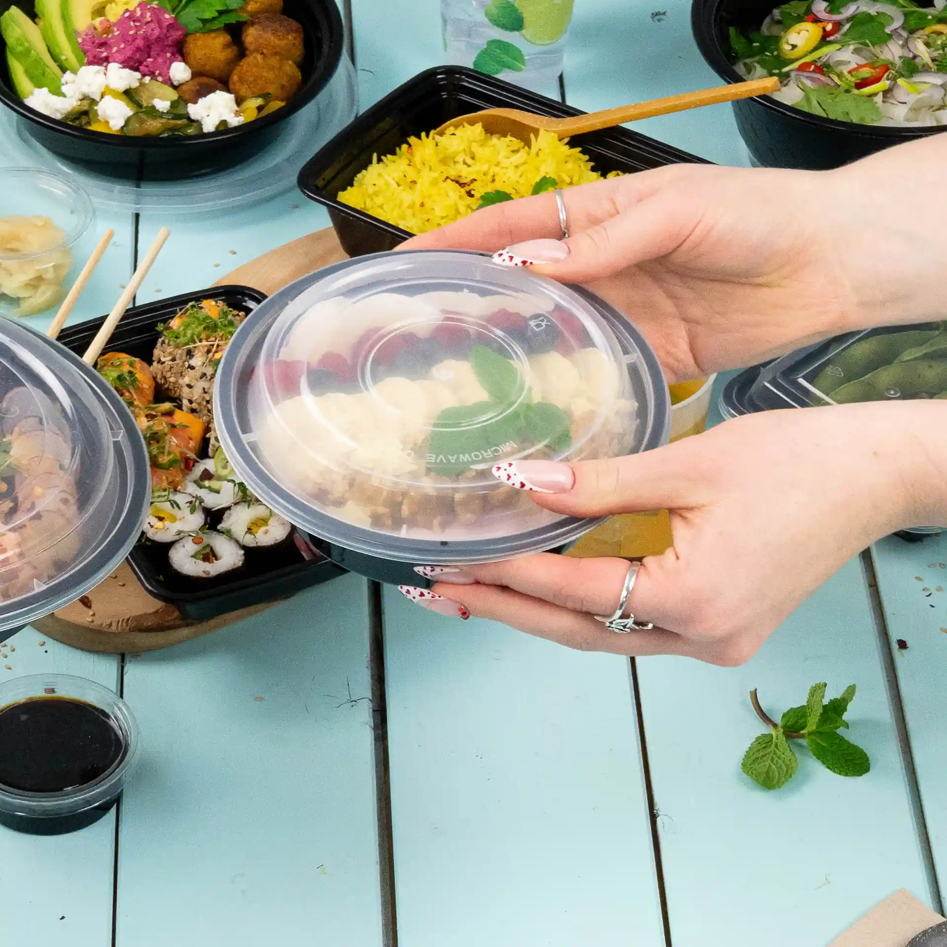 Transparante ronde herbruikbare deksel van polypropyleen, boven een tafel met verschillende voedselcontainers gehouden.