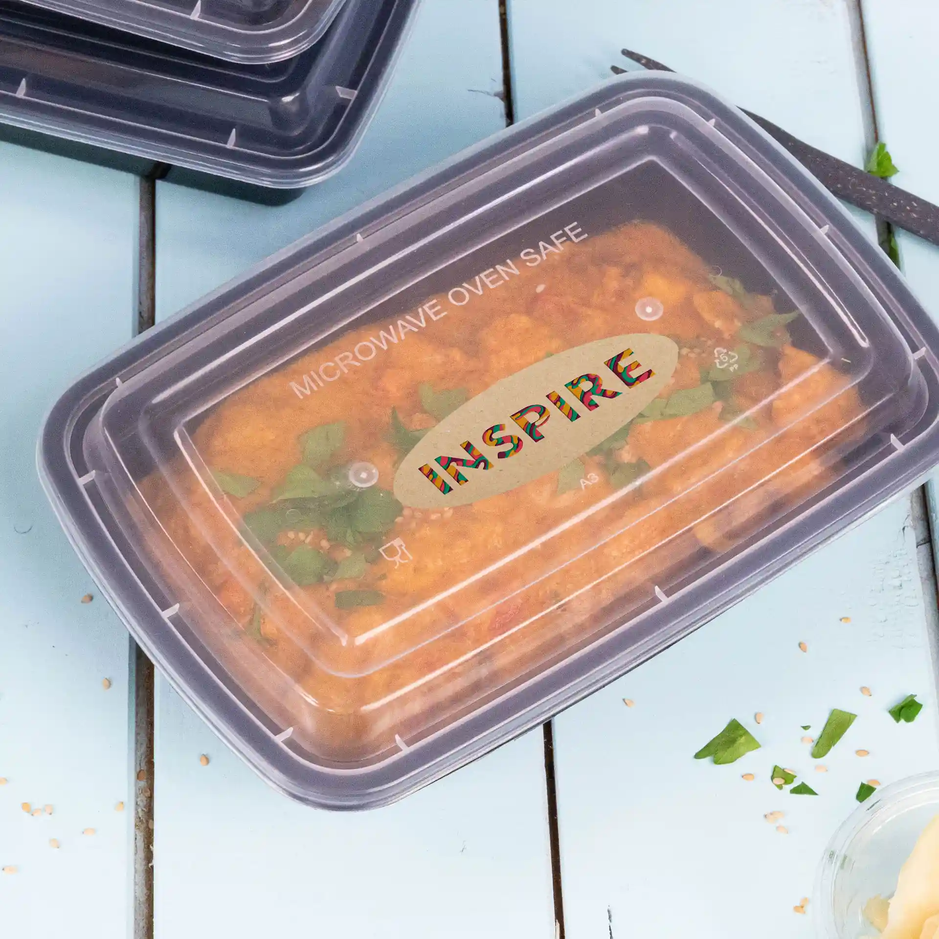 Container met een doorzichtig deksel dat voedsel binnenin toont, gelabeld met "MAGNETRONBESTENDIG" en "INSPIRE" bovenop.