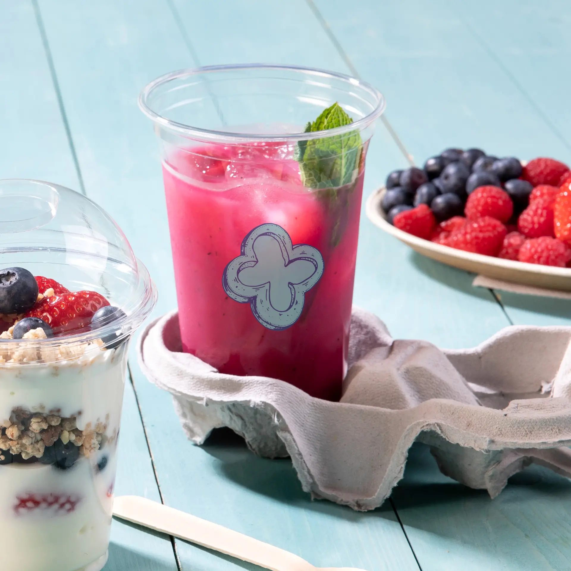 Duidelijke 20 oz rPET-beker met een decoratief blauw etiket, gevuld met een roze drankje en gegarneerd met munt, op een stoffen ondergrond.