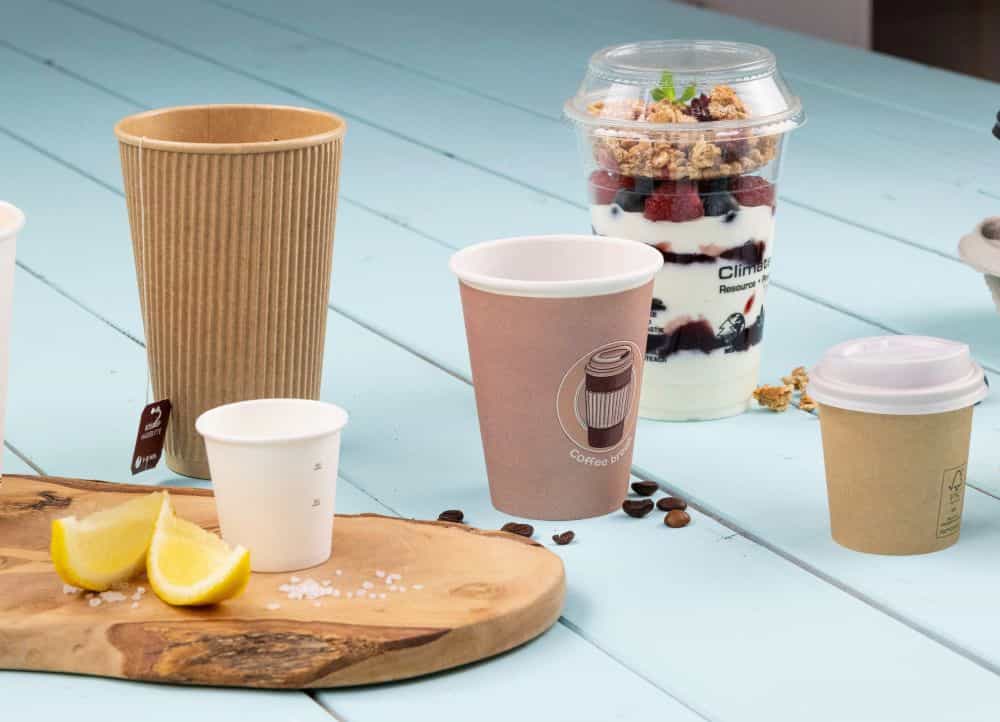 Meerdere wegwerpbekers en een dessert in een doorzichtige beker, met citroenpartjes en zout op een houten plank.