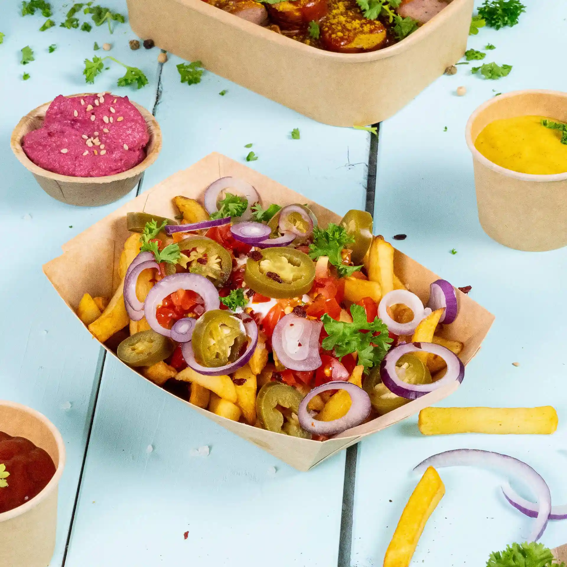 Karton snacktray gevuld met frietjes, tomaten, jalapeños, uien en kruiden op een blauwe ondergrond.