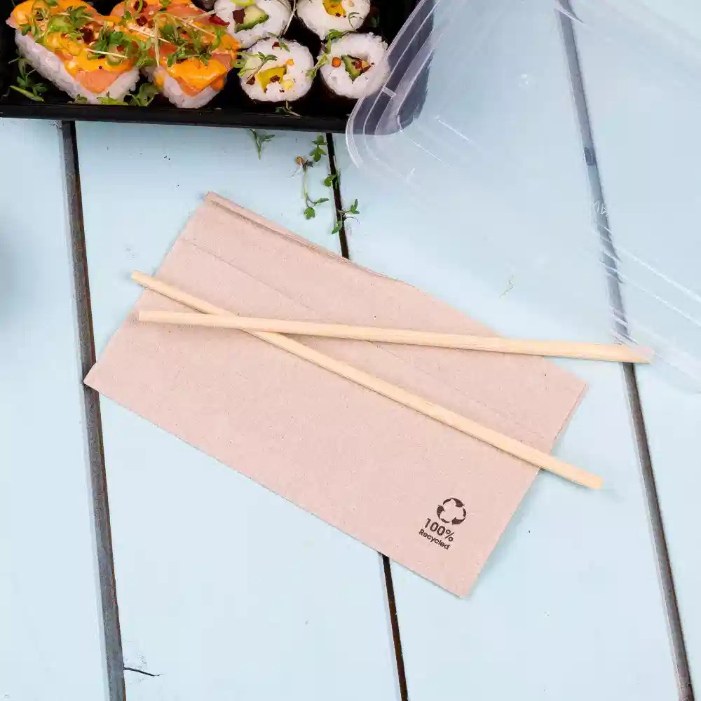 Bruine papieren servetten met houten eetstokjes op een blauwe tafel naast een sushi-container.