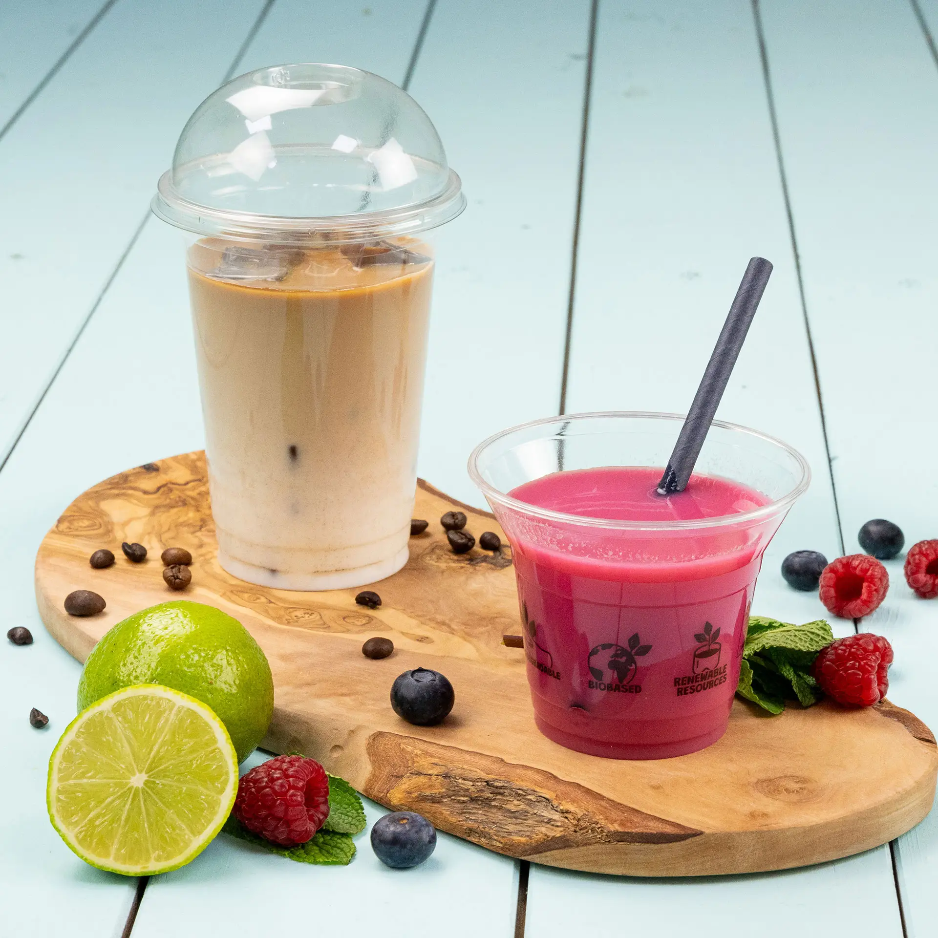Transparante bekers met koude drankjes, waaronder iced coffee en een roze drankje, op een houten serveerplank.
