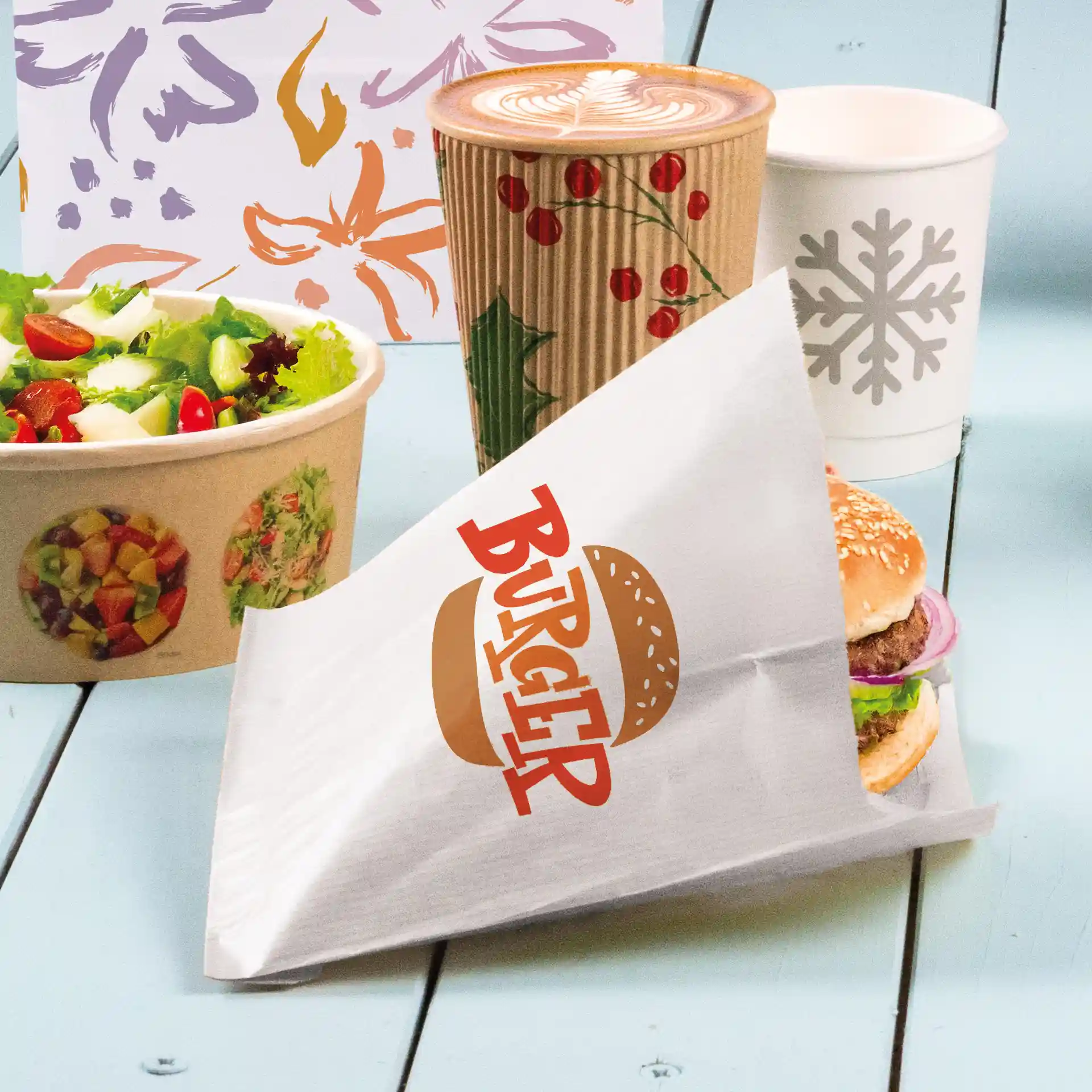 Witte burger sleeve met de tekst "BURGER", houdt een burger met sesambroodje, sla en ui, naast een salade en drankjes.