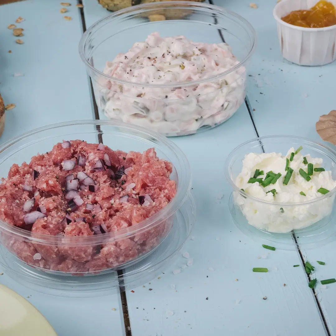 Drie transparante containers met verschillende spreads: roze vleesmengsel met uien, romige witte spread en witte kaasspread met bieslook.