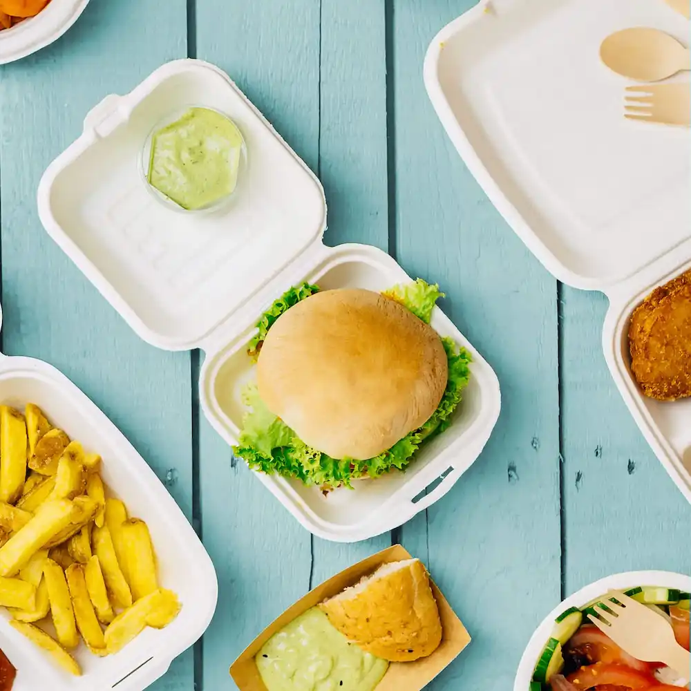 Een enkele hamburger op sla in een witte afhaalcontainer, met frietjes, dipsaus en andere zichtbare voedingsmiddelen.