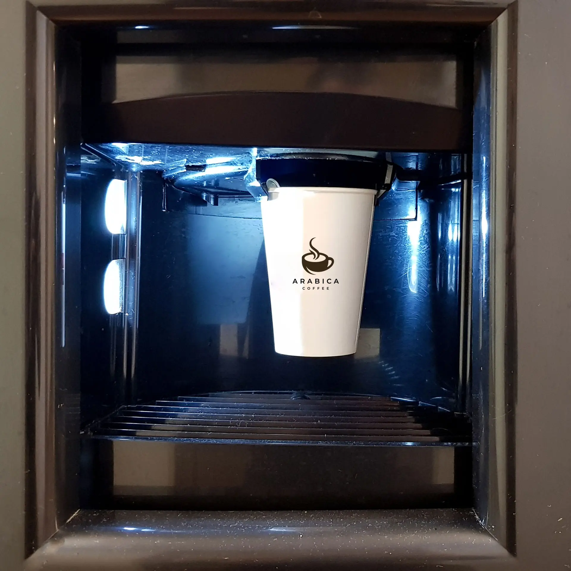 Een witte papieren beker met een "Arabica Coffee"-logo in een dispenser, verlicht door blauwe LED-lampen.