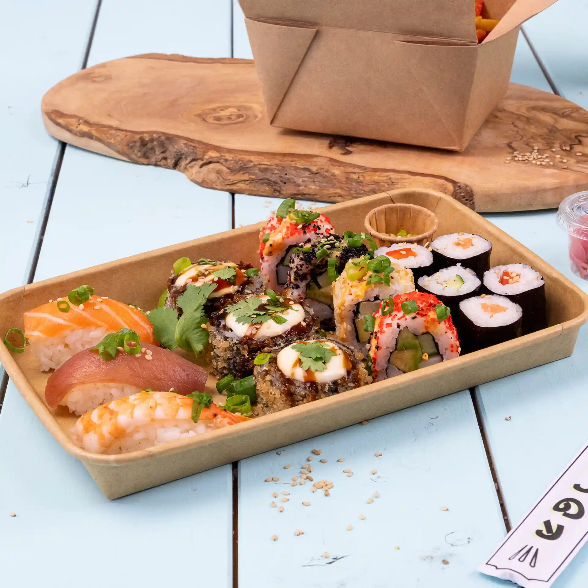 Sushi-assortiment in een bruine PE-gecoate doos, met verschillende rollen en sashimi, op een houten oppervlak.