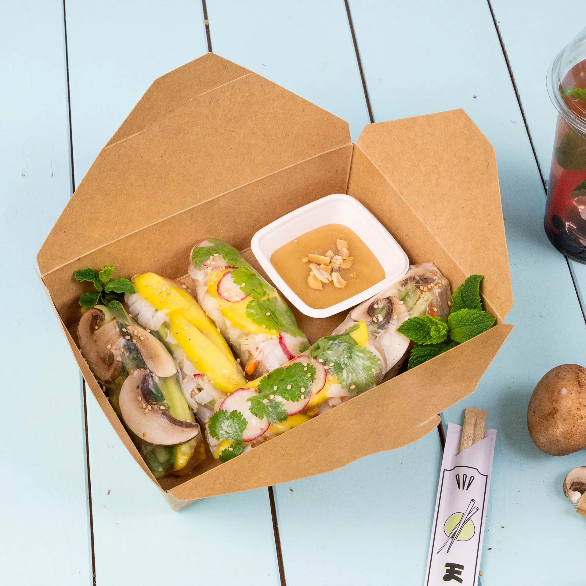 Bruine kartonnen wegwerpdozen met een opvouwbaar deksel; inclusief chopsticks, salade en dip in een houten setting.