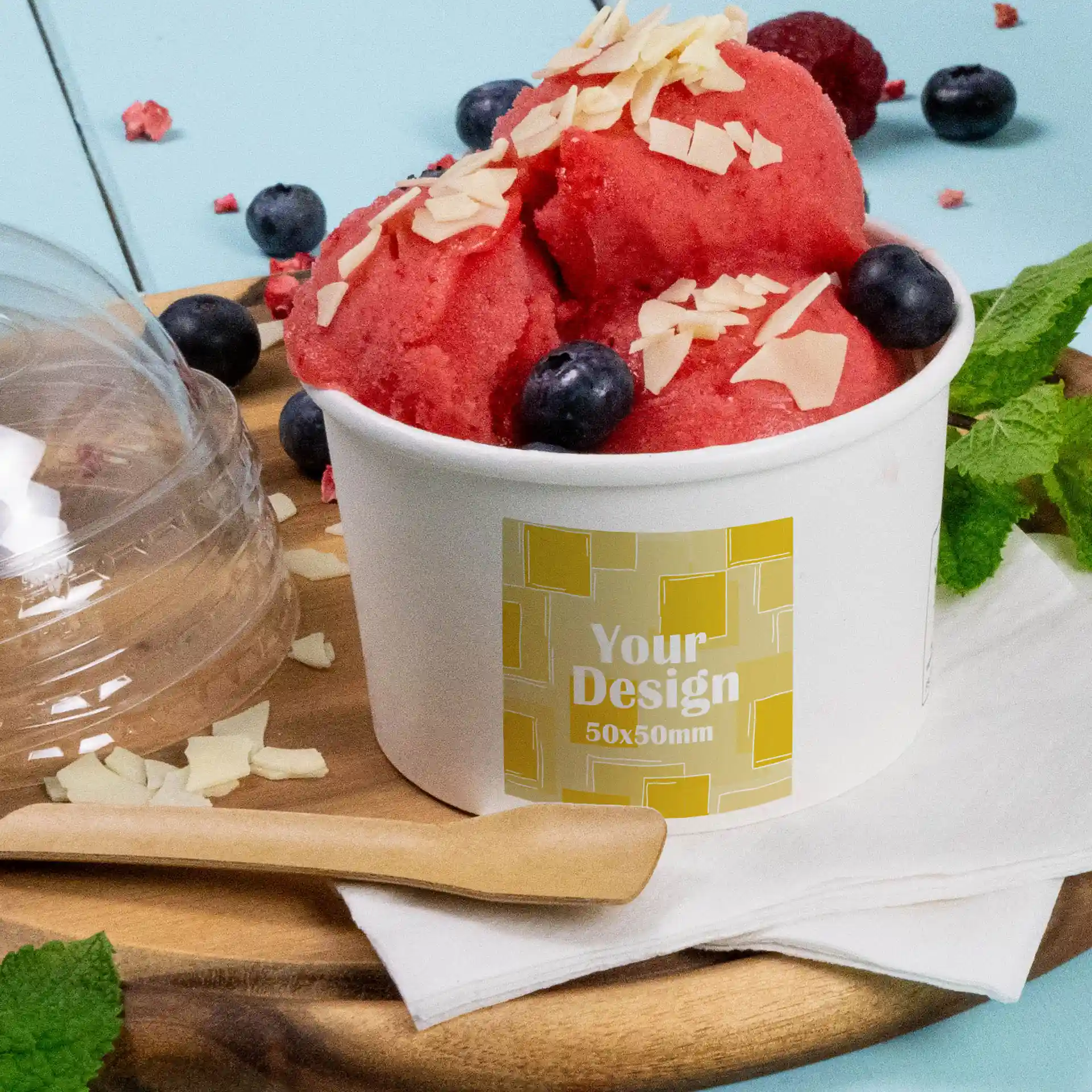 Beker met rode sorbet, getopt met amandelschaafsel en bosbessen, met een geprint label op een witte matte container.