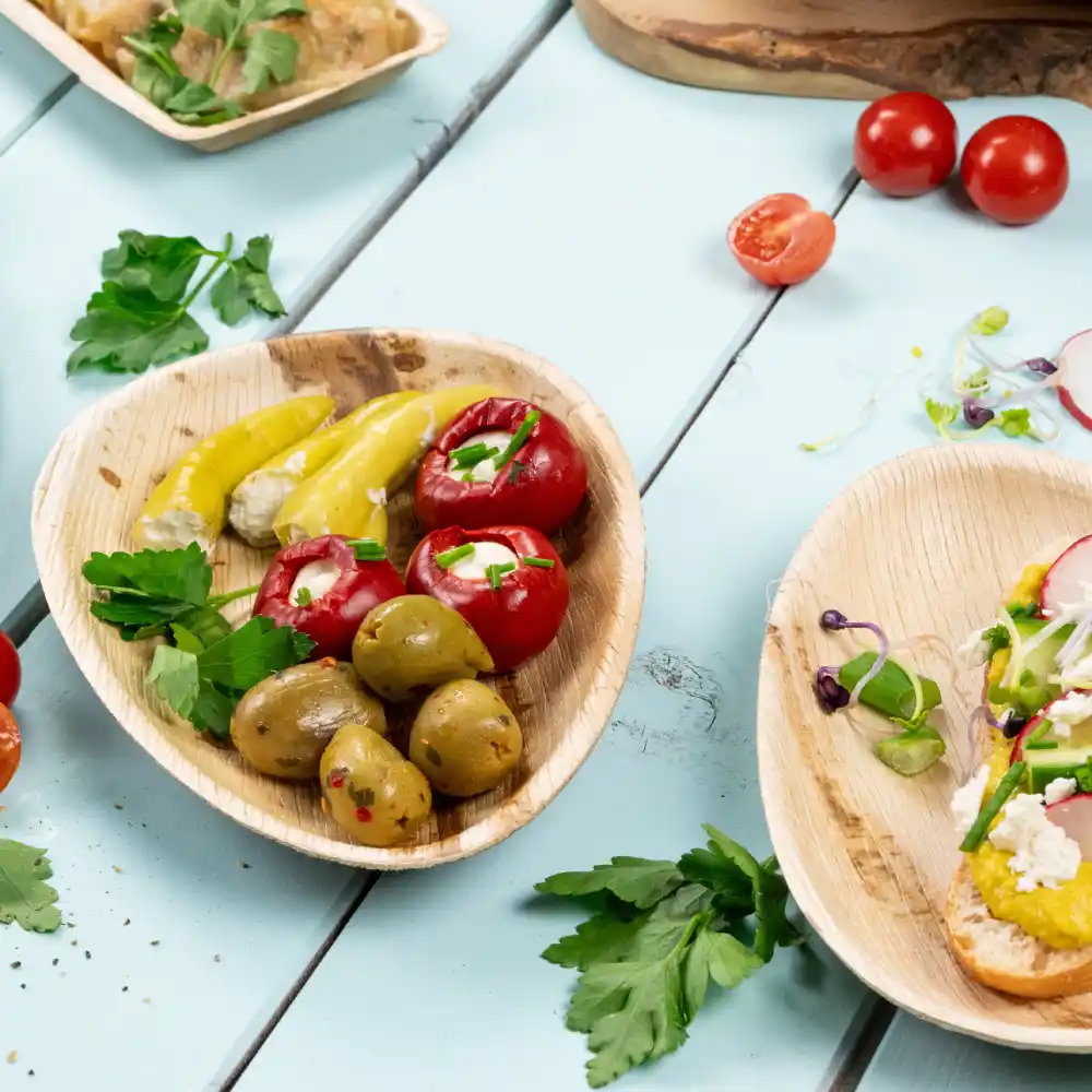 Een houten bord met gevulde rode paprika's, ingelegde gele paprika's en groene olijven; verse kruiden verspreid over een blauwe ondergrond.