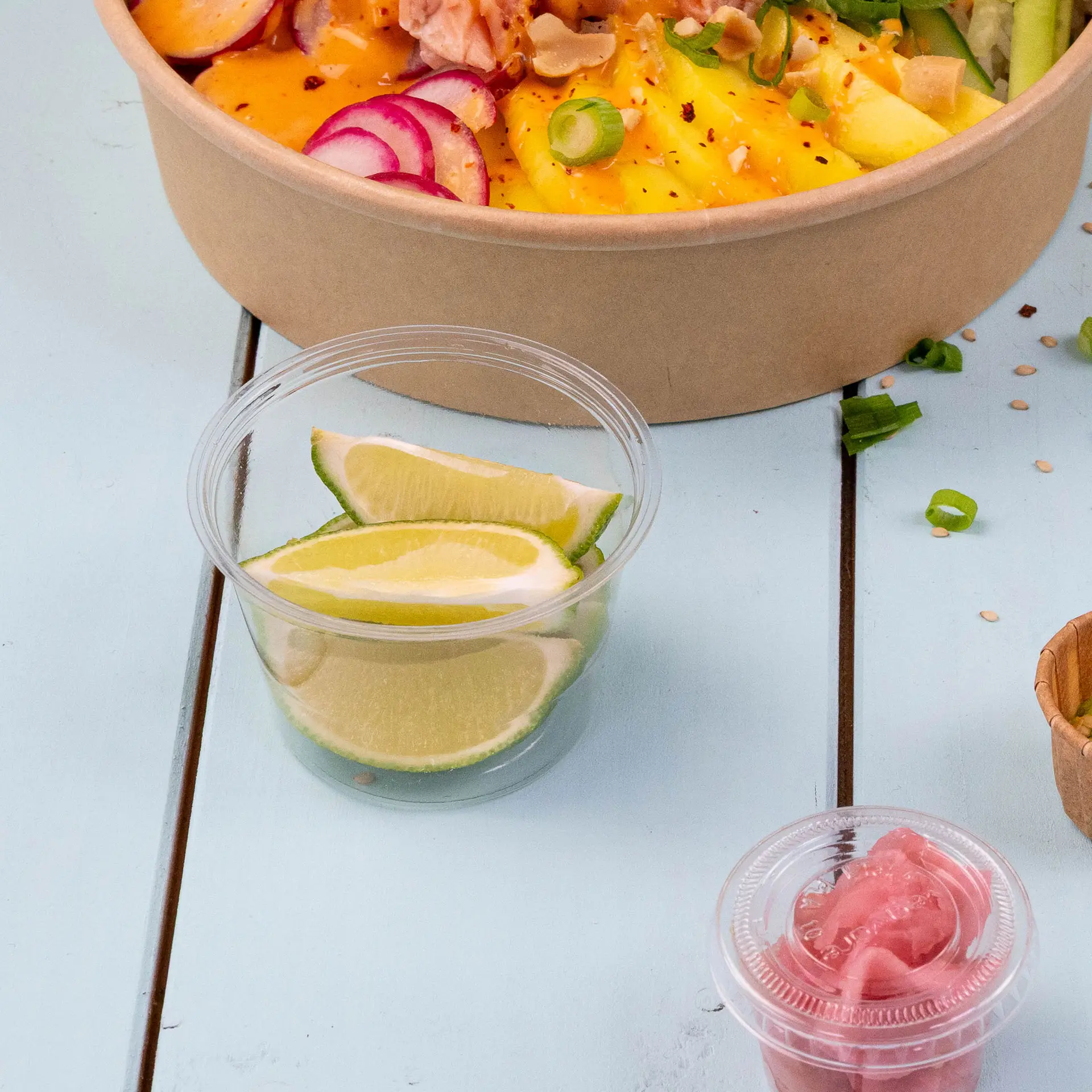Duidelijke PLA bio-portie bekers met limoenpartjes voor dressing of dip, geplaatst naast een kom salade.