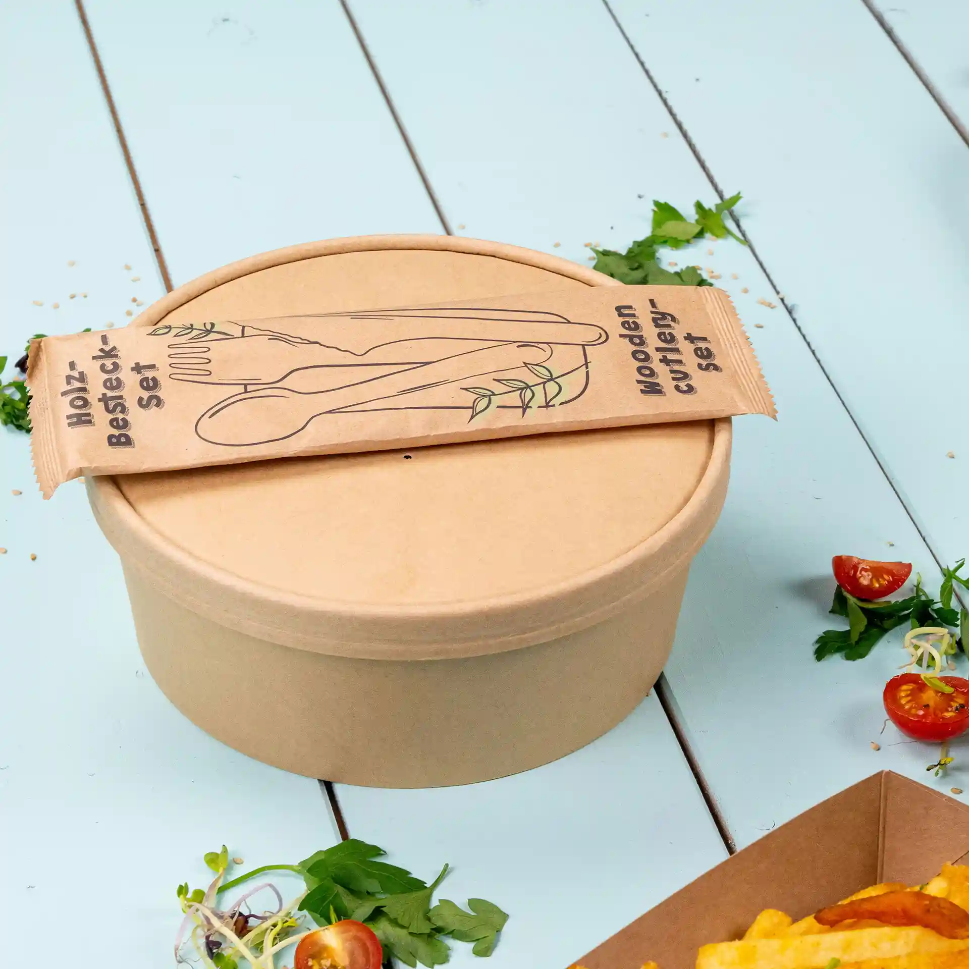 Bruine ronde papieren kom met deksel, verpakt met een set houten bestek.