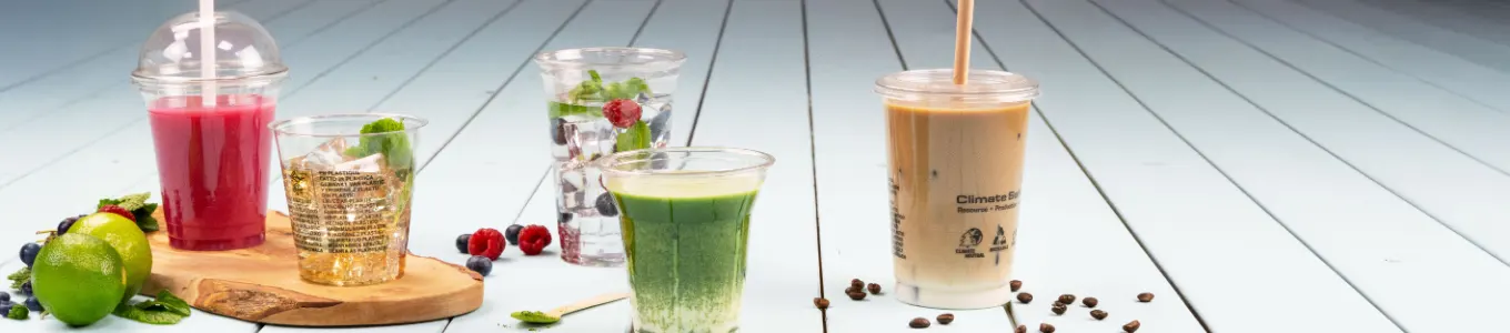Diverse dranken gepresenteerd op een houten oppervlak, waaronder iced coffee, smoothie, yoghurtparfait en sap, met een schijfje sinaasappel erbij.
