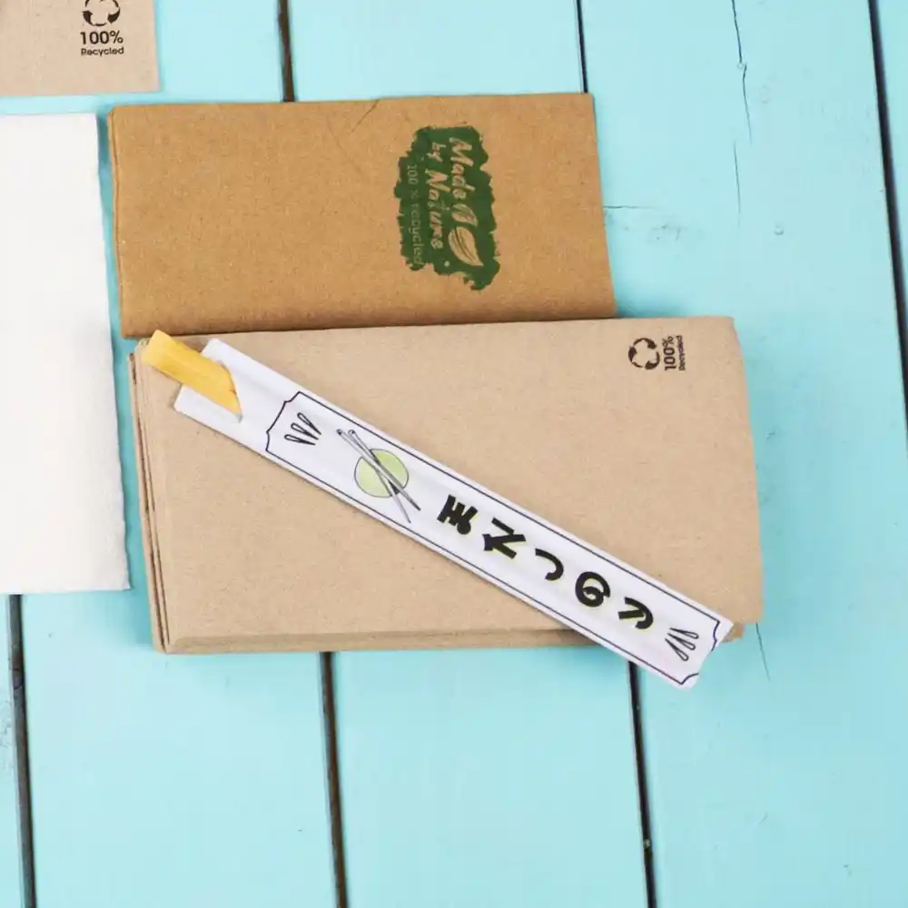Chopsticks gewikkeld in papier op een blauwe houten ondergrond, met een bruine kraftpapierdoos op de achtergrond.