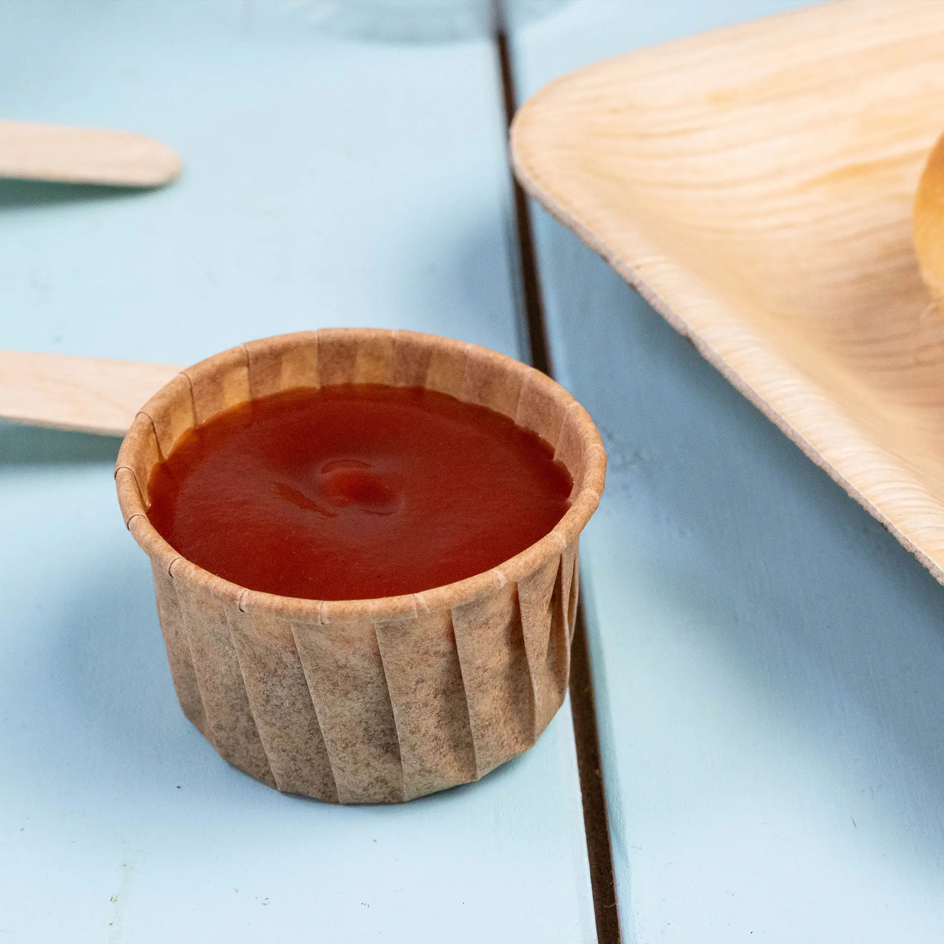 Bruin papieren dipbeker gevuld met ketchup op een blauwe ondergrond, ontworpen voor sauzen en kleine porties.