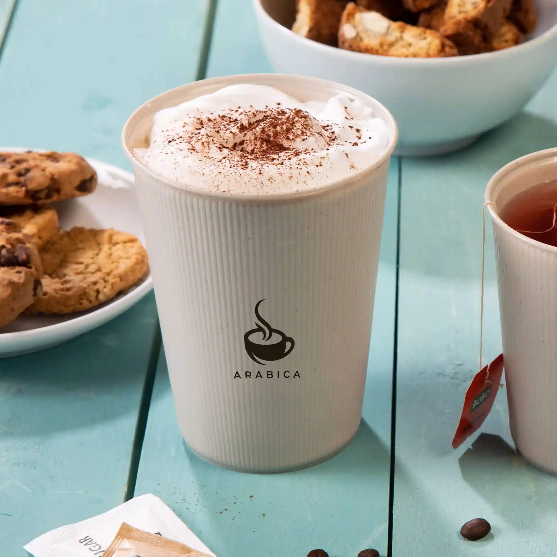 Herbruikbare beker met een golvend ontwerp, gevuld met slagroom en cacaopoeder, naast koekjes en thee.