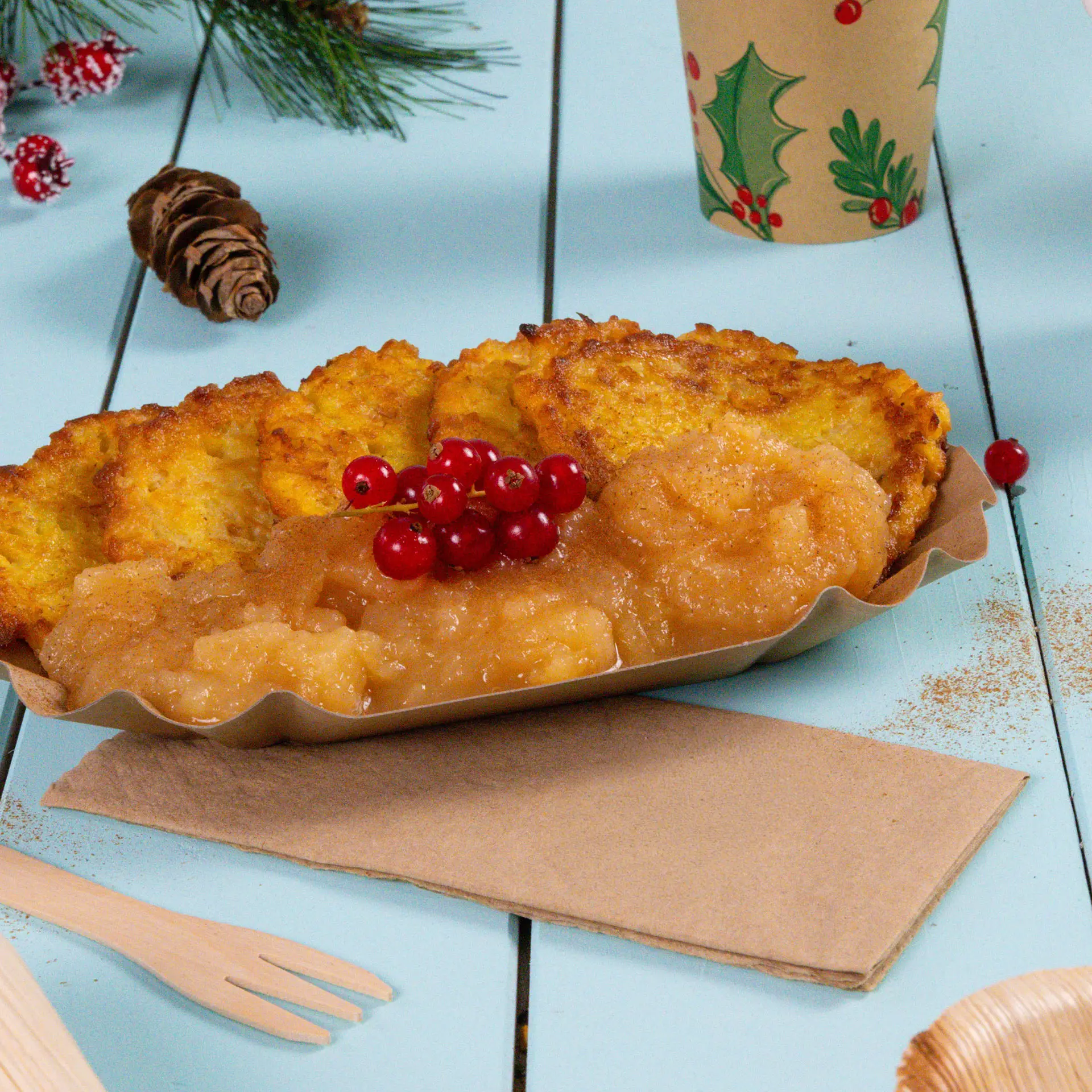 Bord met verschillende goudbruine fritters, appelmoes en rode bessen, op een lichtblauw houten oppervlak met een servet.