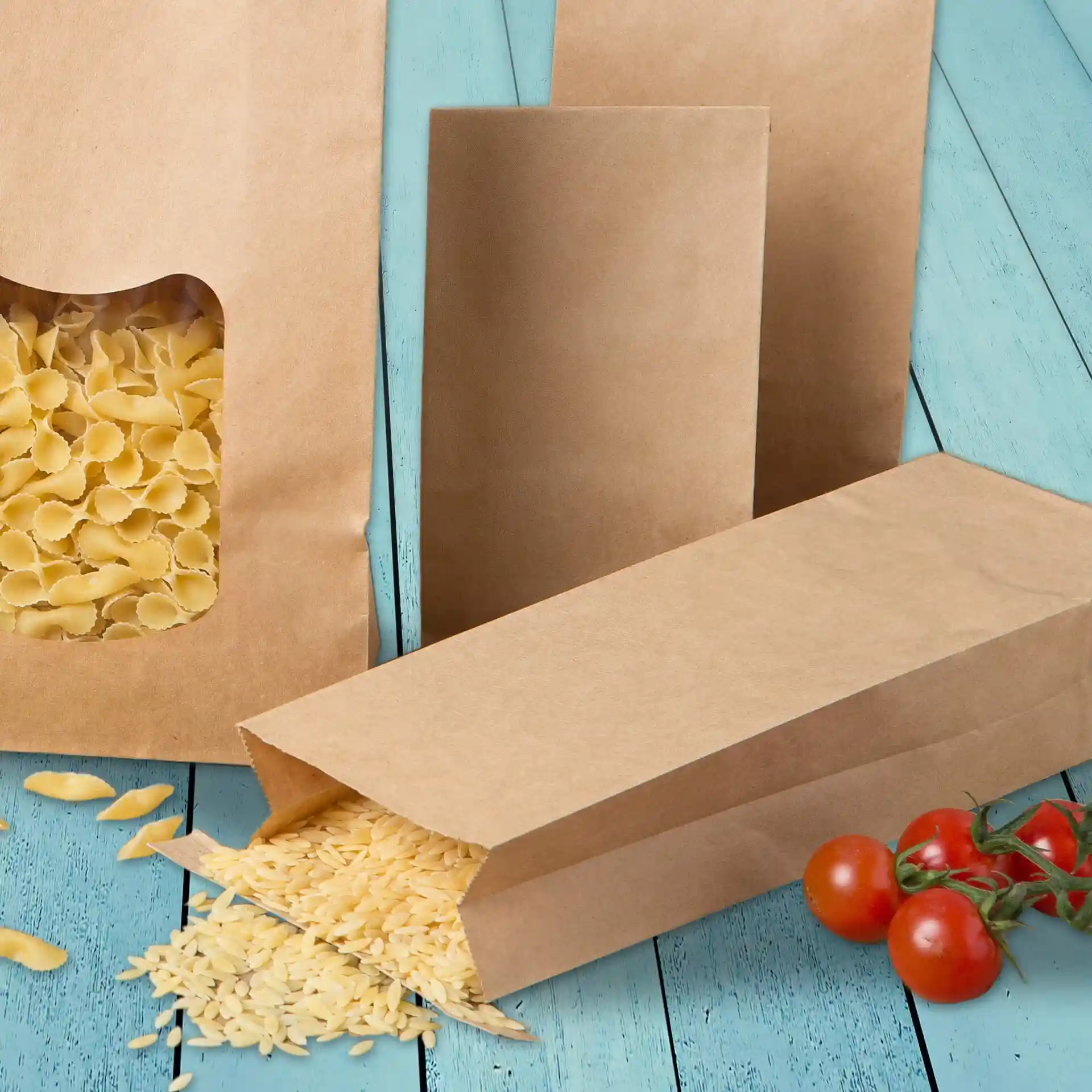 Bruine blokbodemtassen met pasta die eruit valt, op een blauwe houten ondergrond, naast cherrytomaten.