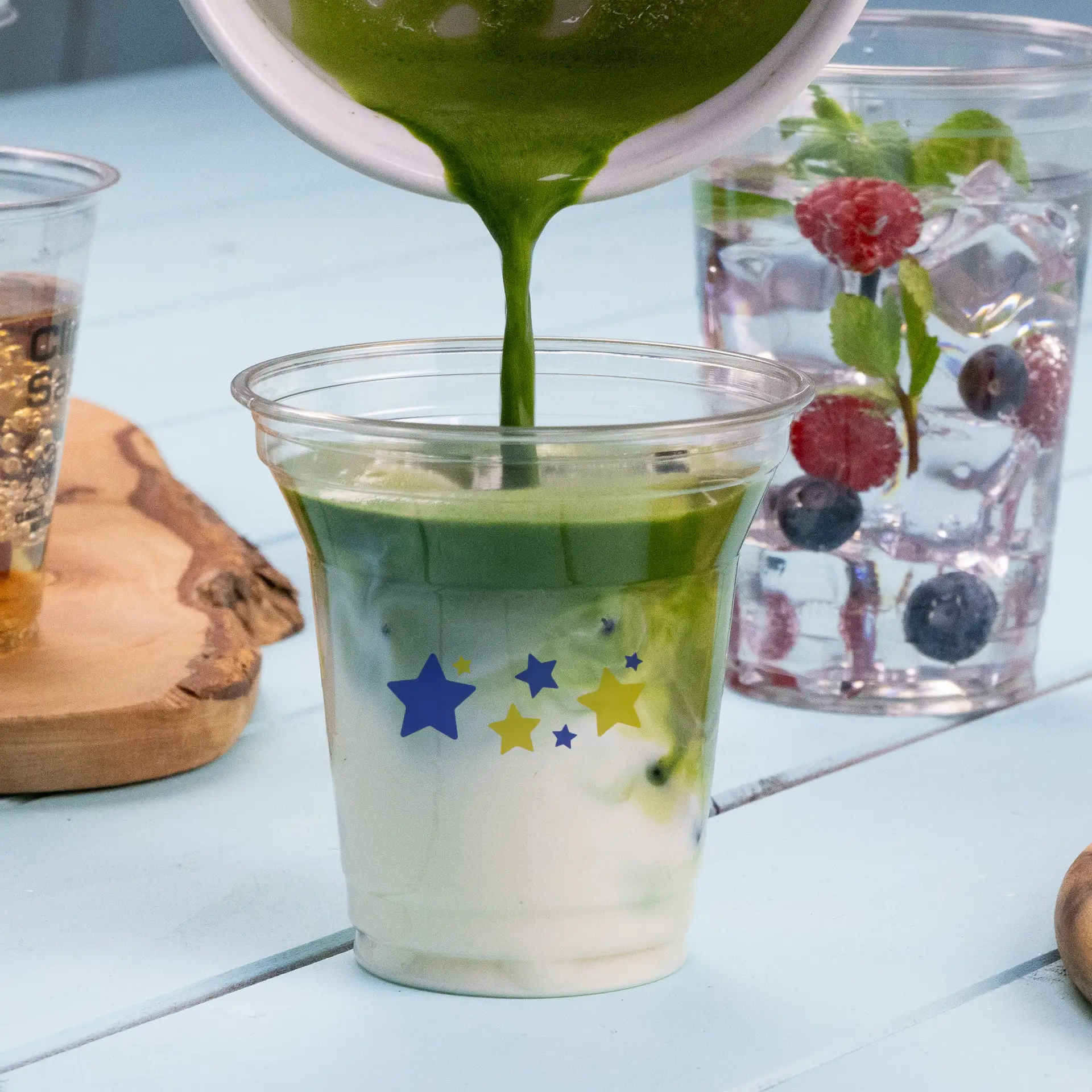 Groene drank in een 8 oz rPET heldere beker met sterontwerpen gieten; andere dranken op de achtergrond.