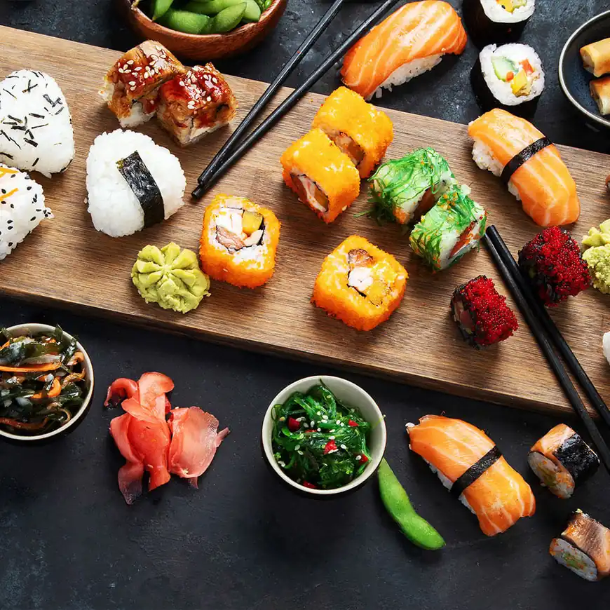 Een houten schaal met verschillende soorten sushi, waaronder rollen, sashimi en nigiri. Vergezeld van wasabi, ingemaakte gember en kleine kommetjes zeewiersalade.