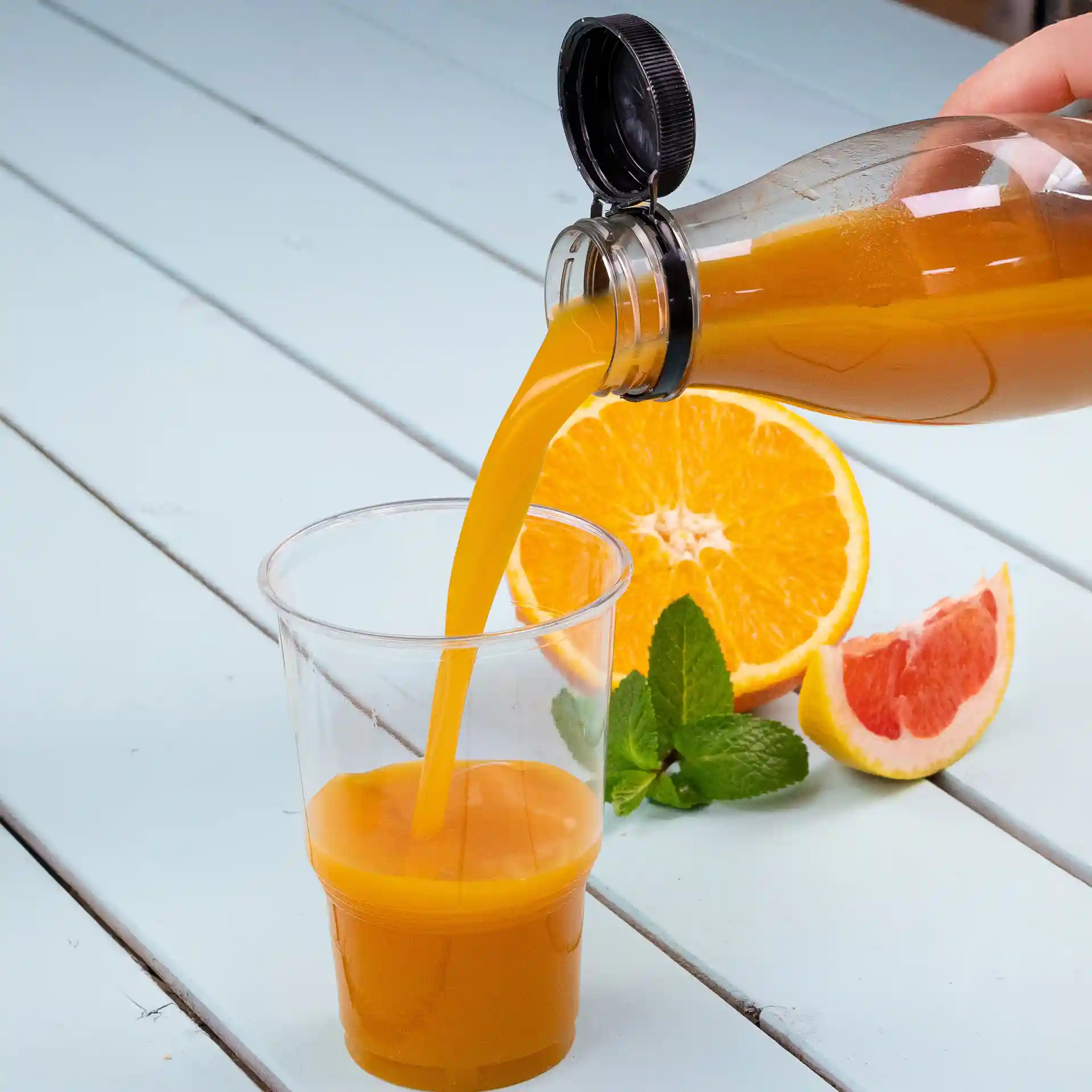 Transparante rPET-fles die sinaasappelsap in een heldere beker giet, met sinaasappel- en grapefruitplakken erbij.