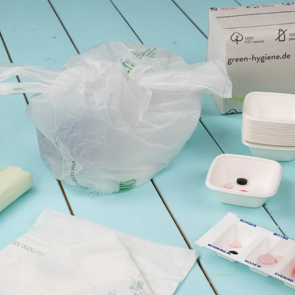 Plastic zak met hygiëneproducten; een witte kom met verschillende artikelen en een doos met het etiket "green-hygiene.de" in de buurt.