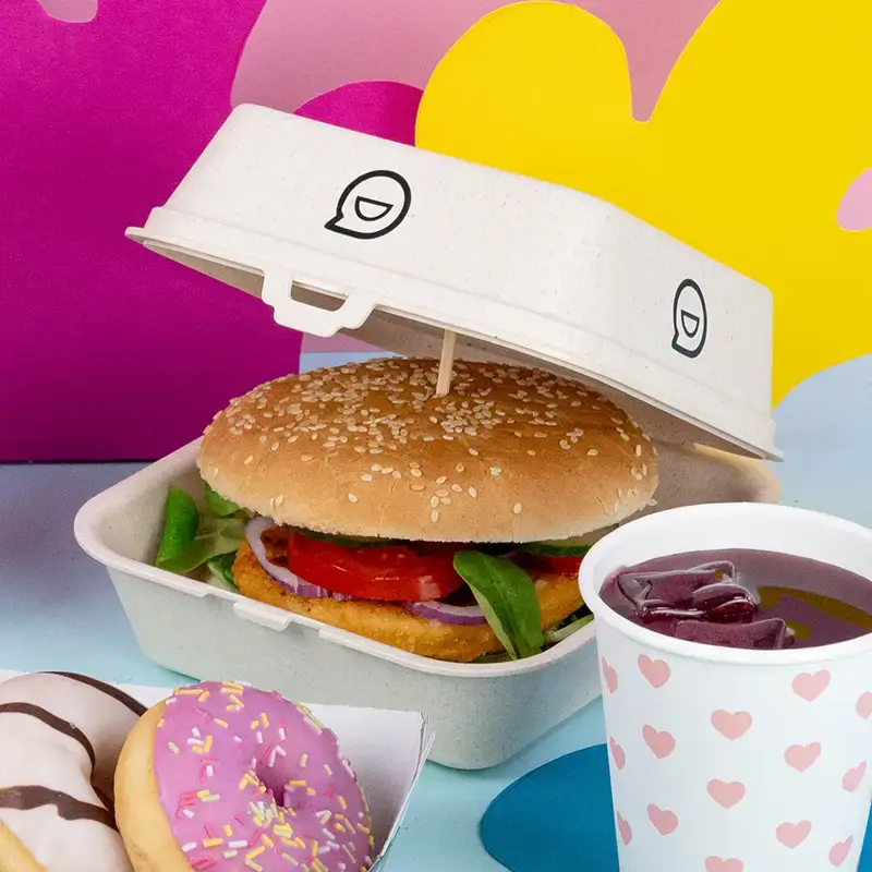 Bruine takeaway-doos met aanpasbare ontwerpt tekst, geplaatst op een blauwe houten ondergrond met peterselie en ander servies.