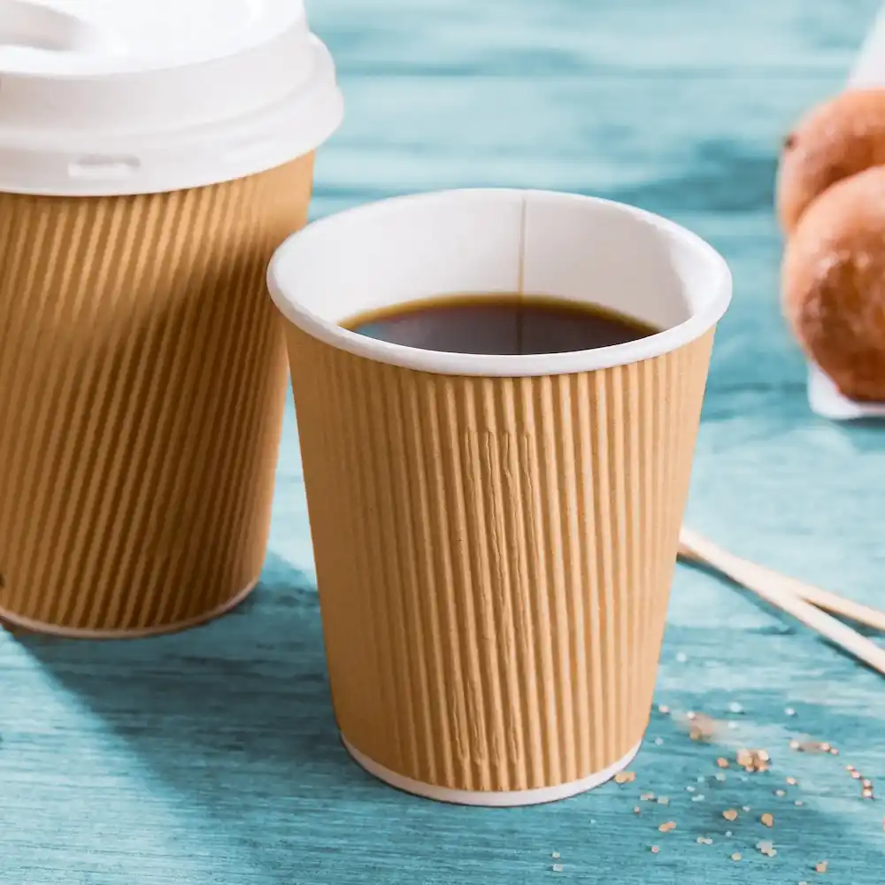 Bruine geribbelde papieren beker met zwarte koffie, naast een vergelijkbare beker en donuts op een blauwe ondergrond.