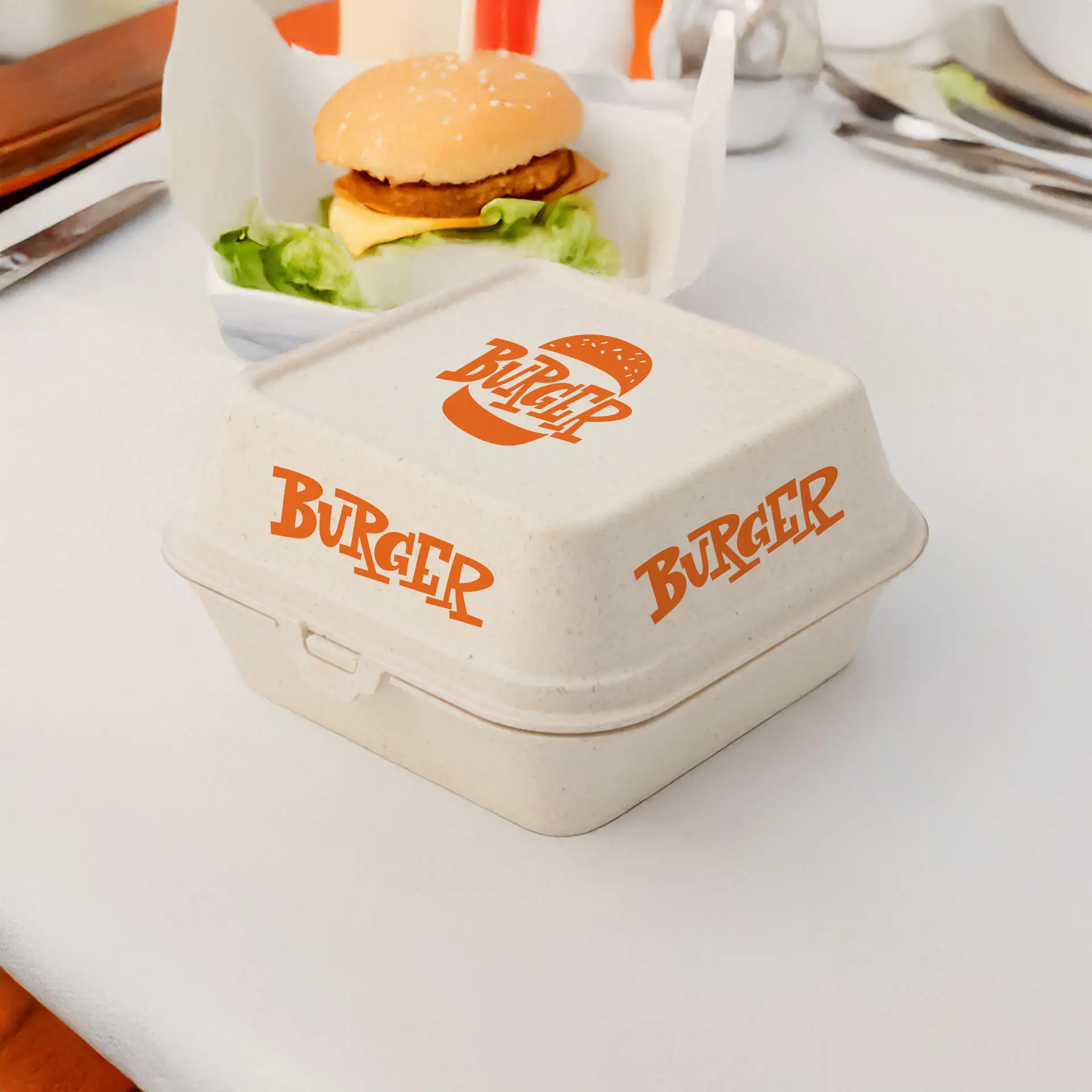 Crèmewitte herbruikbare burgerdoos met oranje "BURGER"-logo, geschikt voor warme en koude etenswaren, naast een hamburger op een tafel.