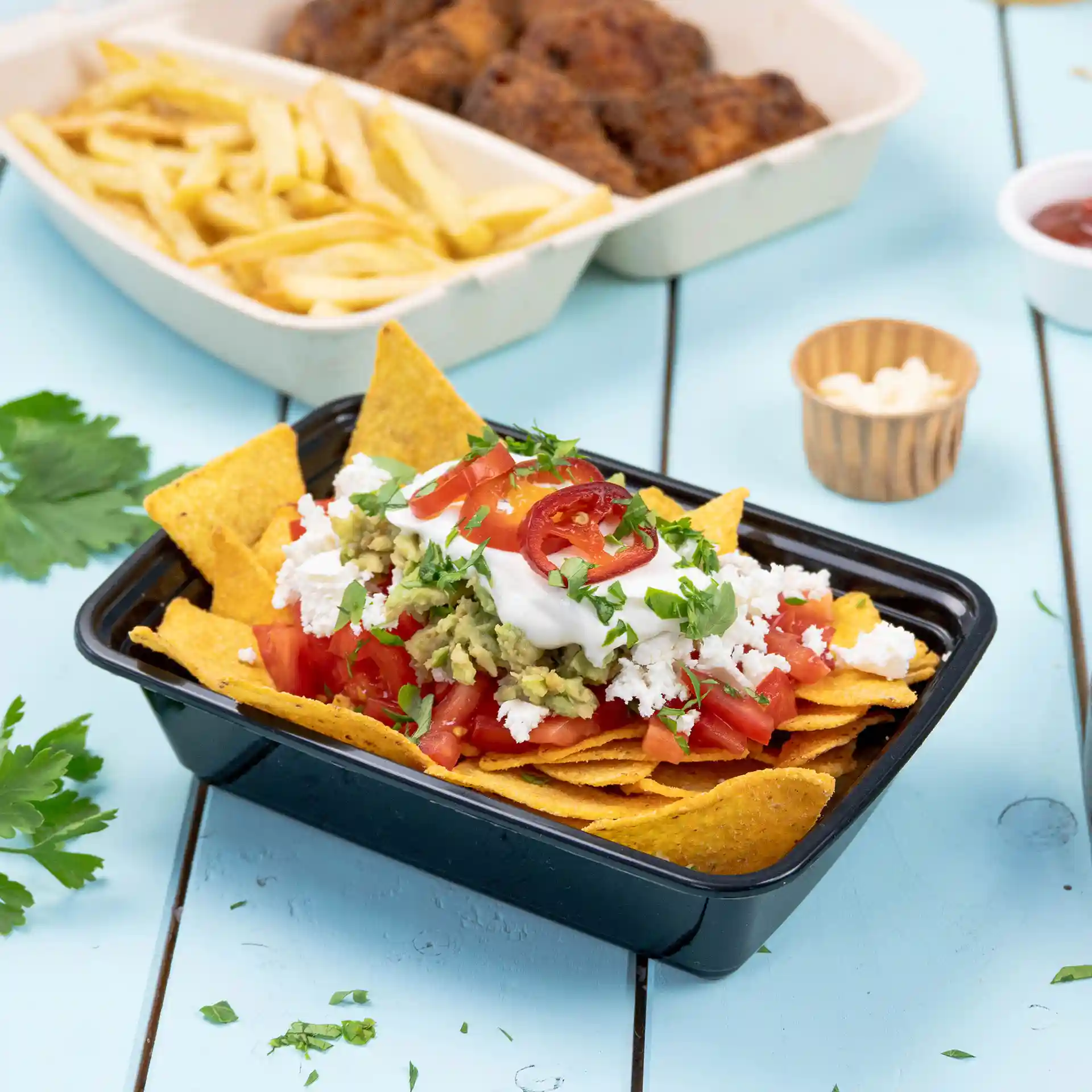 Zwarte rechthoekige herbruikbare container gevuld met nacho's, getopt met tomaten, guacamole, zure room en koriander.