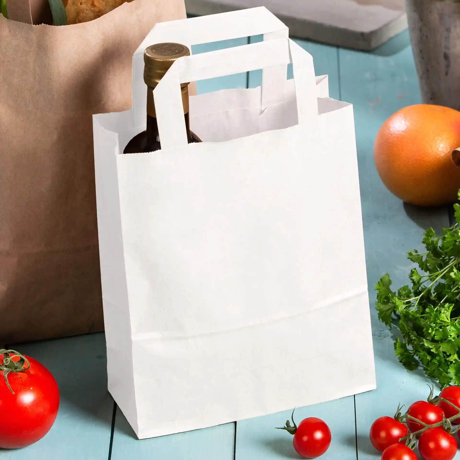Witte kraftpapieren tas met handvatten, met een fles, omringd door tomaten en een sinaasappel op een blauwe ondergrond.
