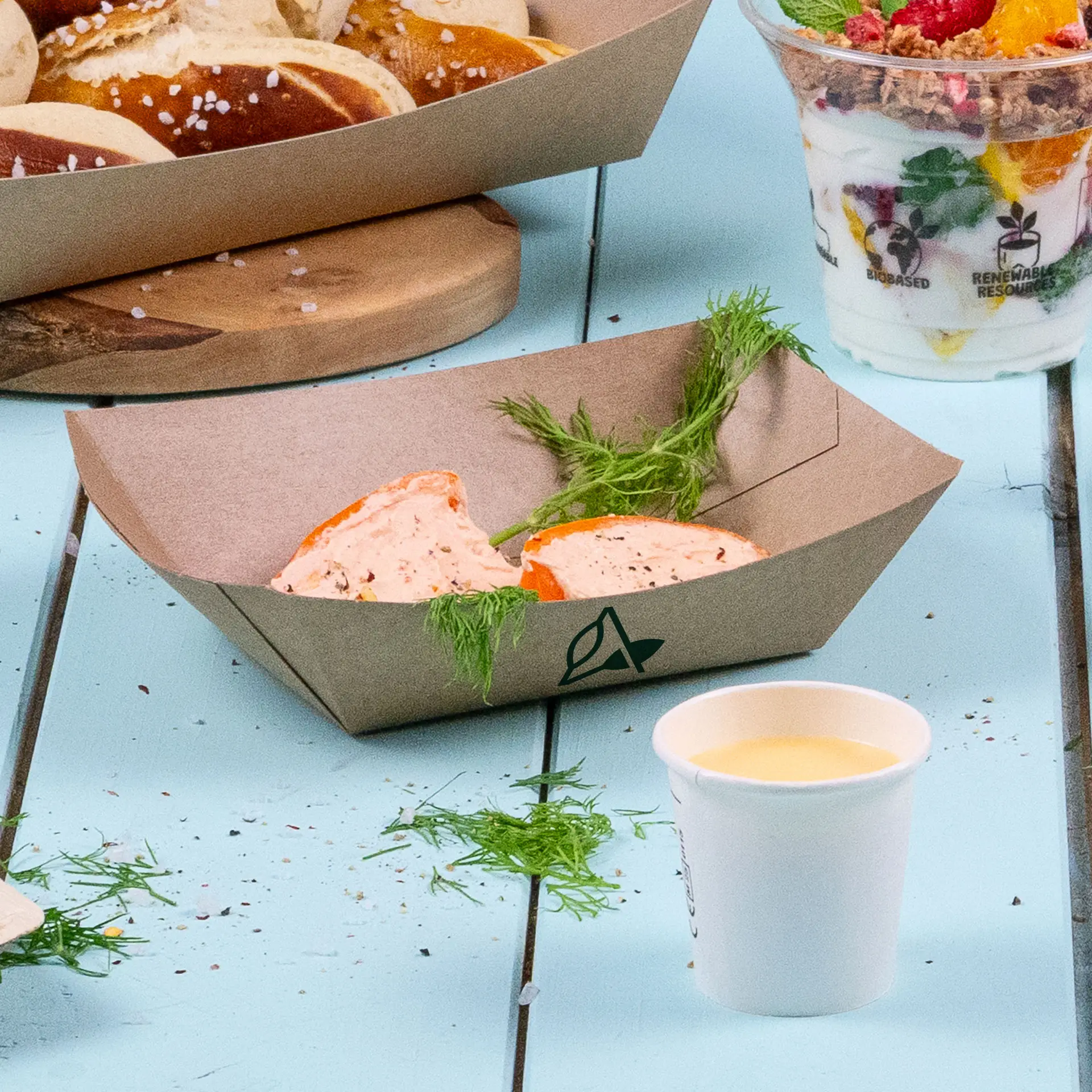 Een bruin snacktray met PLA-coating met twee porties dip; dichtbij staat een beker en meerdere pretzels op een tray.