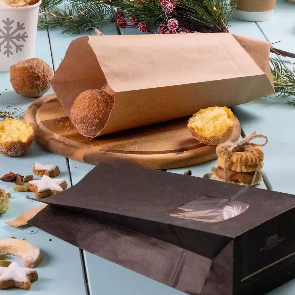 Bruine papieren tas met gebakken producten, zwarte tas met een venster, houten serveerplank en feestelijke versieringen.
