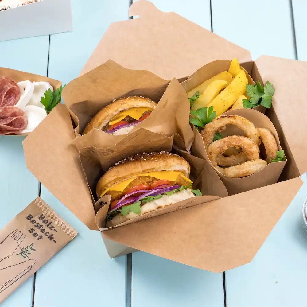 Twee hamburgers met kaas, sla, tomaat en ui in een afhaaldoos, vergezeld van uienringen en frietjes.