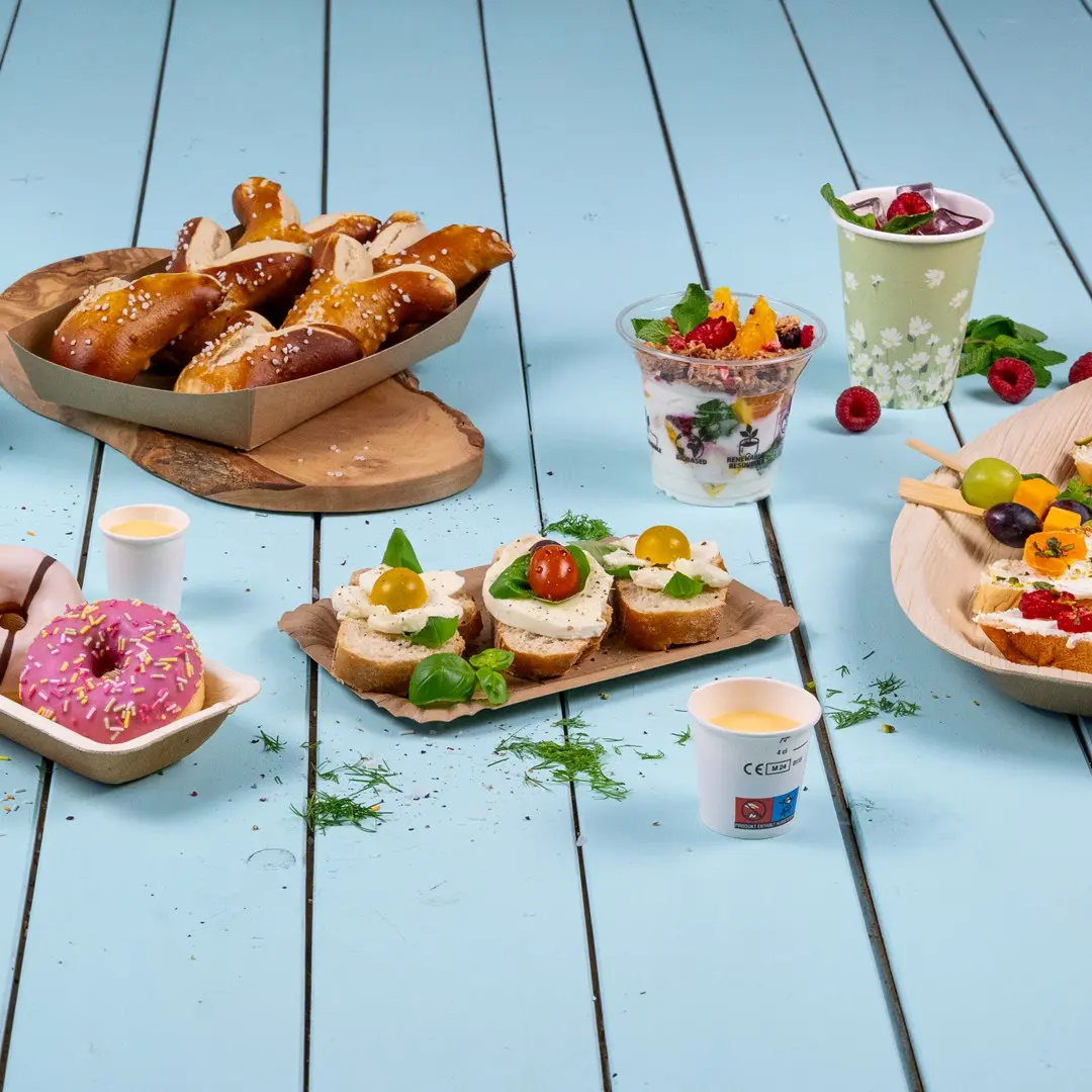 Diverse snacks, waaronder pretzels, sandwiches met toppings, yoghurt parfait, donuts en fruitskewers op een blauwe houten ondergrond.
