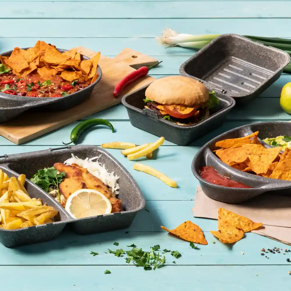 Verscheidenheid aan voedsel in herbruikbare containers, inclusief nacho's, een burger, friet en vis met citroen, op een blauwe ondergrond.
