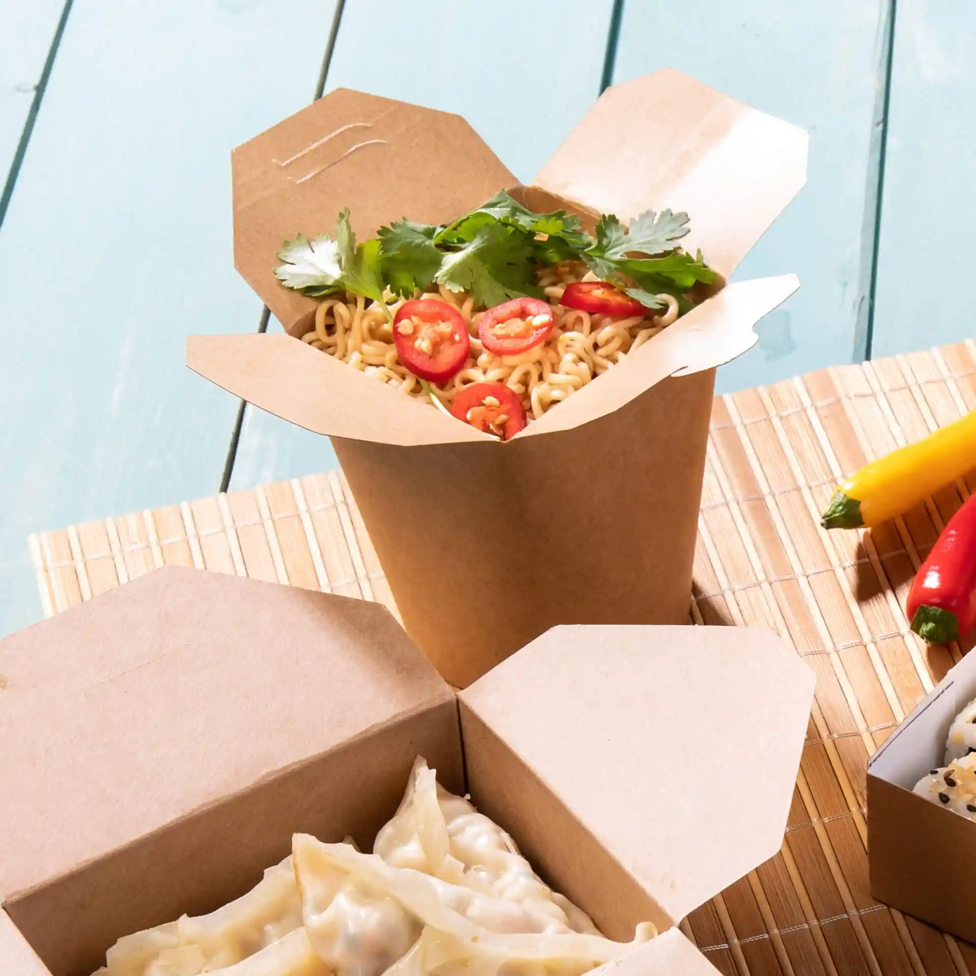 Bruine noedelbox gevuld met noedels, getopt met gesneden chili en koriander, op een bamboemat.