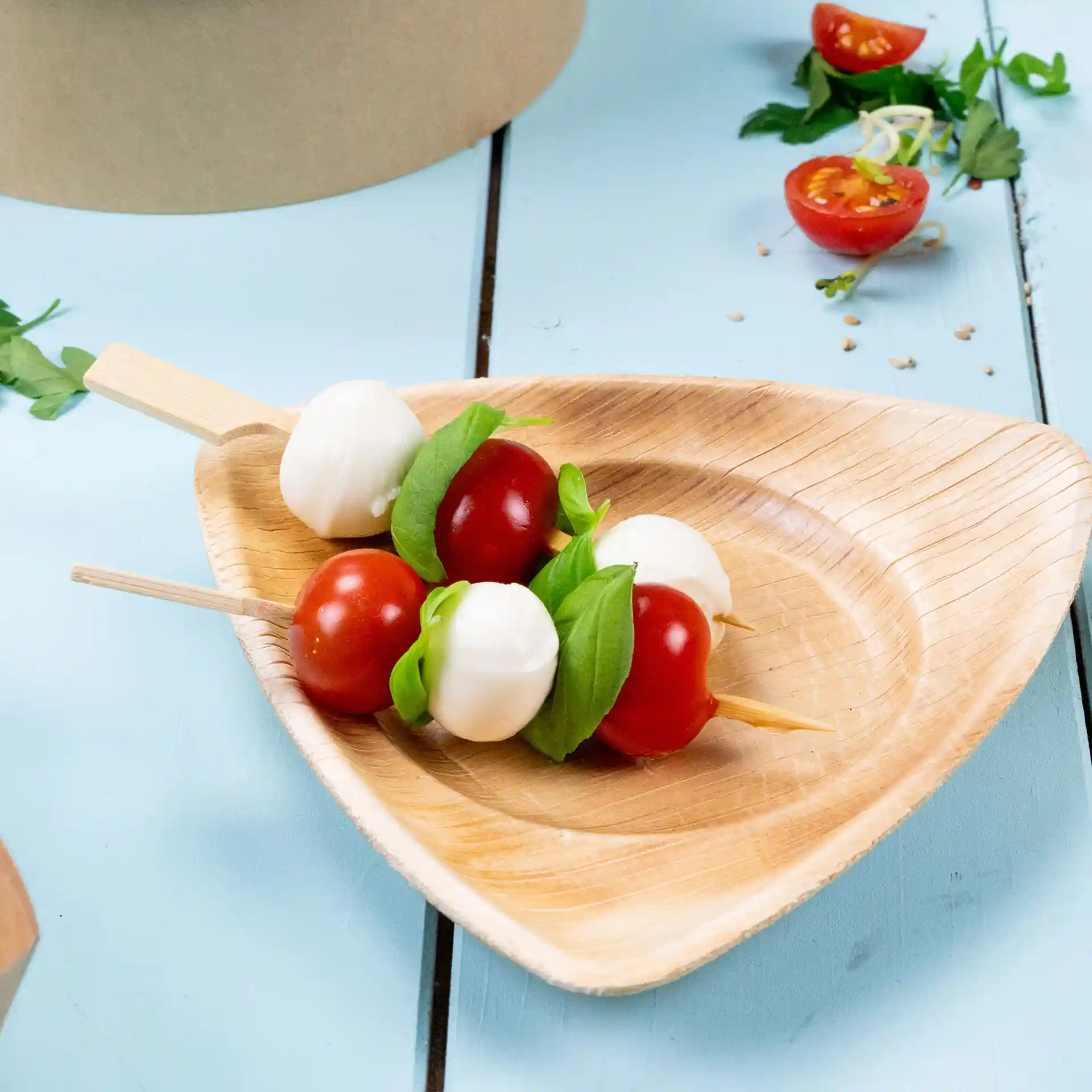 Bamboespiesjes met cherrytomaatjes, mozzarella-balletjes en basilicum op een driehoekig houten bord.