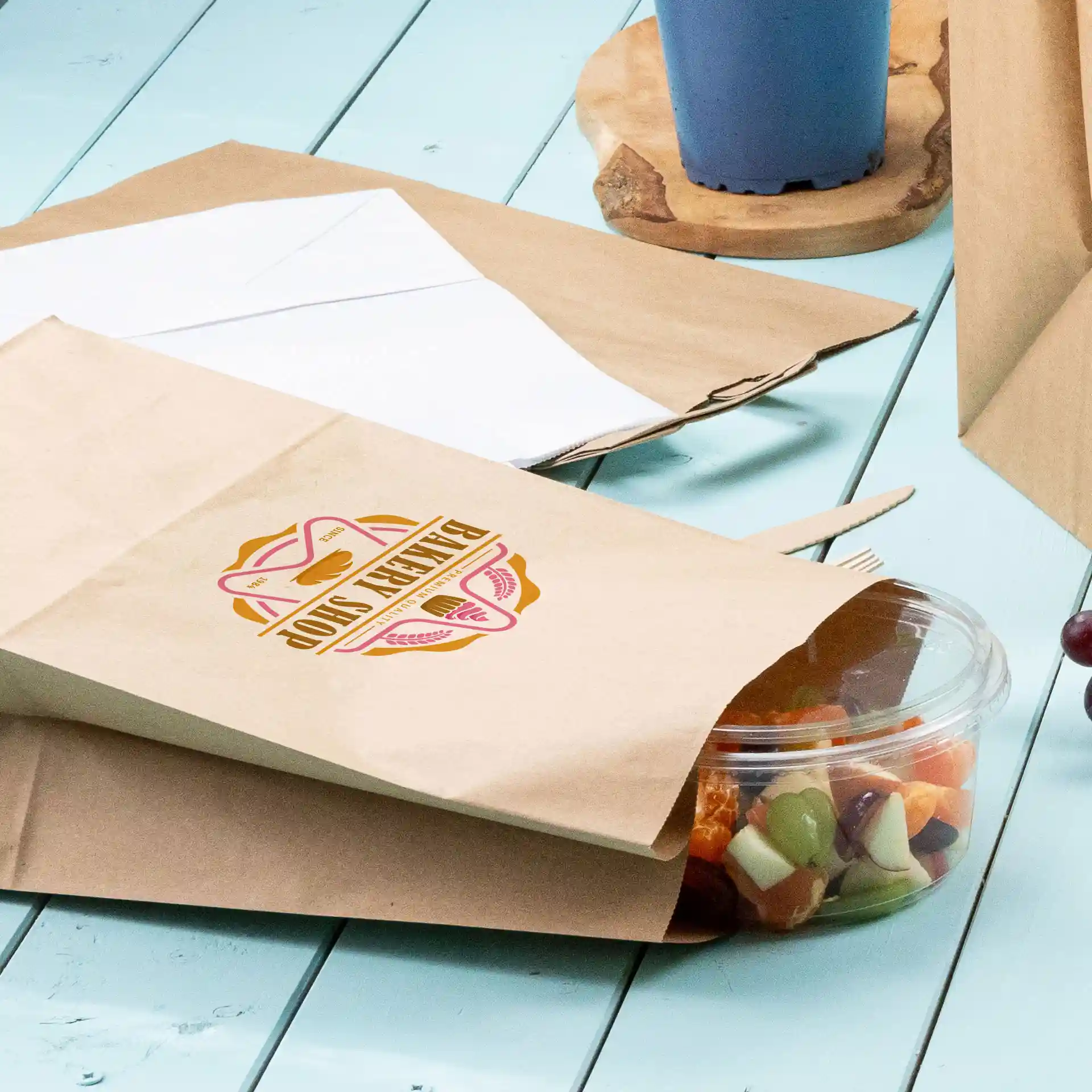 Bruine papieren tas met een groen, rond ontwerp, gedeeltelijk open met een doorzichtige container met gemengd fruit ernaast.