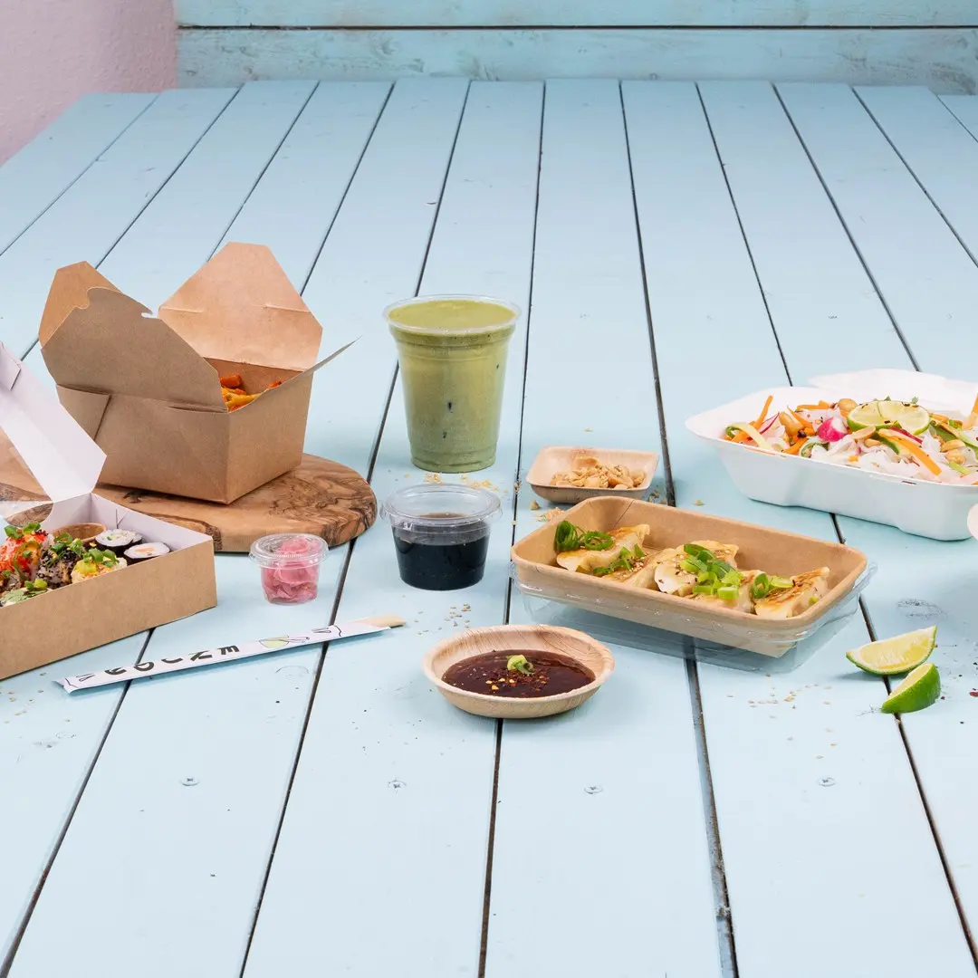 Diverse Aziatische voedingsmiddelen op een blauwe houten tafel, waaronder sushi, dumplings, salade en een groene drank.