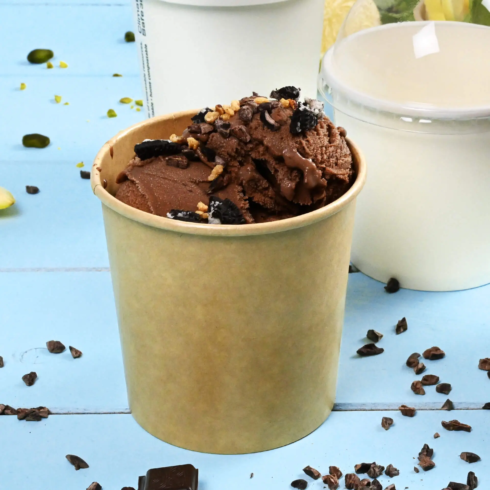 Een bruine papieren ijsbekertje gevuld met chocolade-ijs en toppings, geplaatst op een blauwe ondergrond met verspreide toppings.