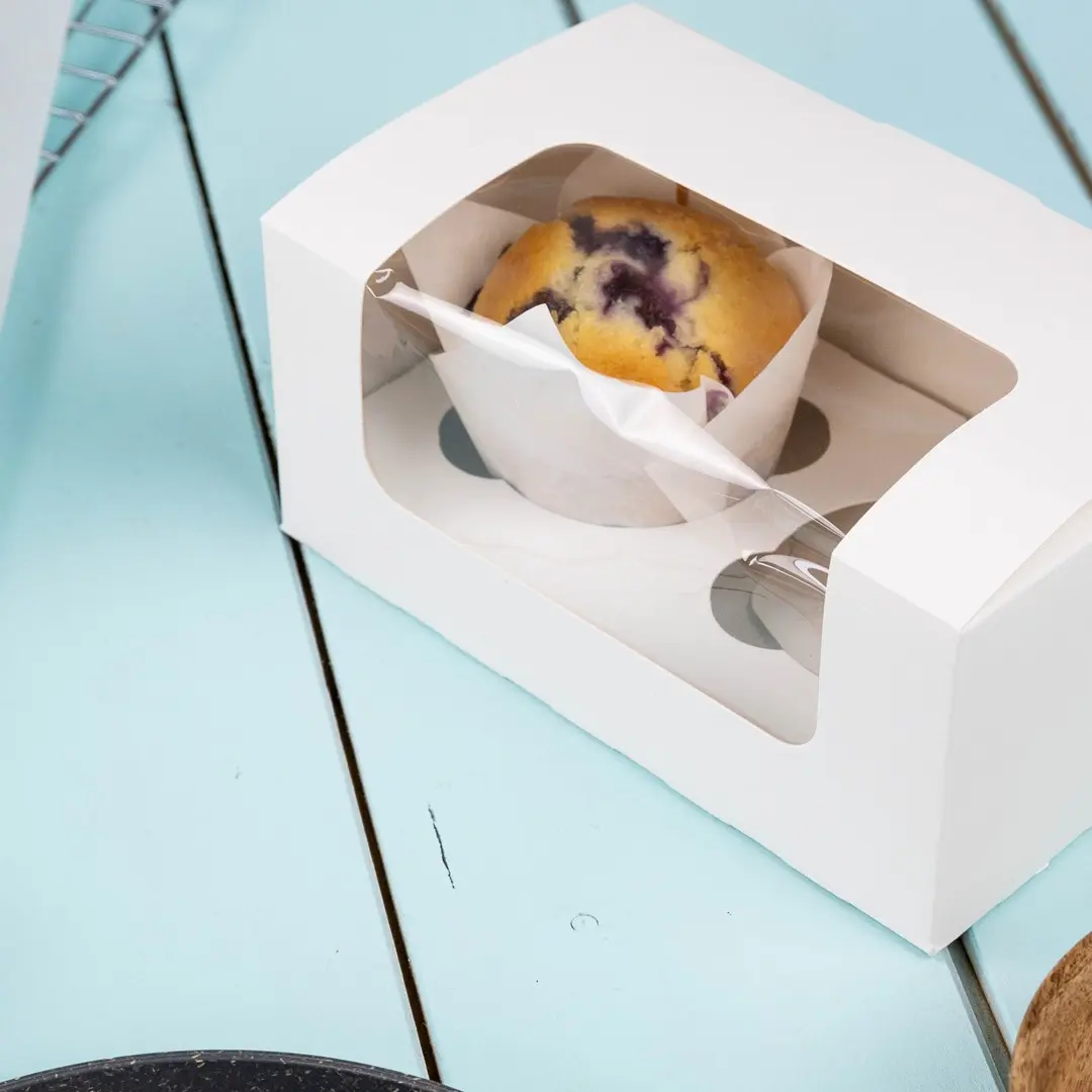 Witte cupcake-doos met een helder venster dat een bosbessenmuffin toont.