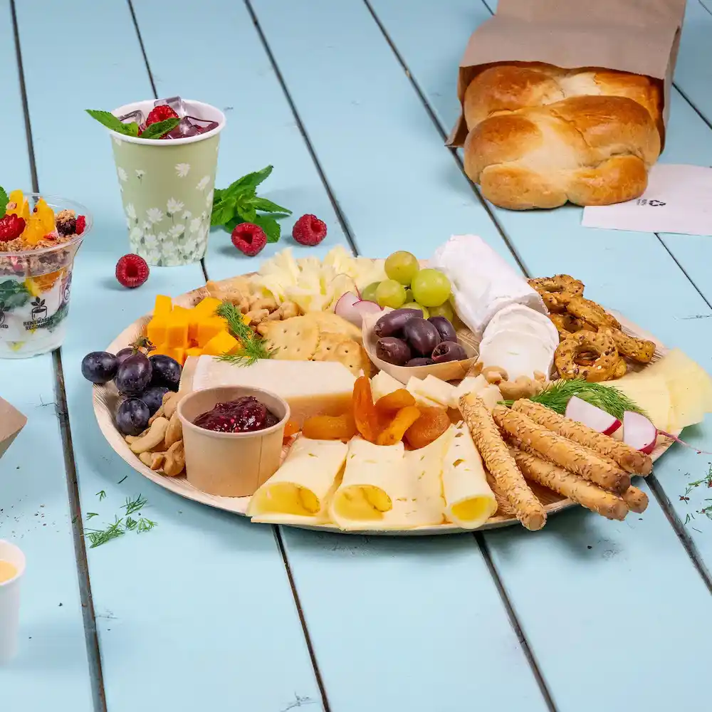 Plank met assortiment aan kazen, crackers, fruit, noten en brood op een blauwe houten ondergrond.