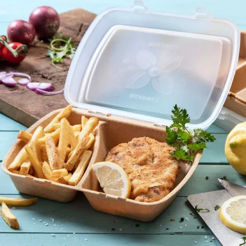 Container met gefrituurde kip, een partje citroen en friet, omringd door voedselitems en een snijplank.