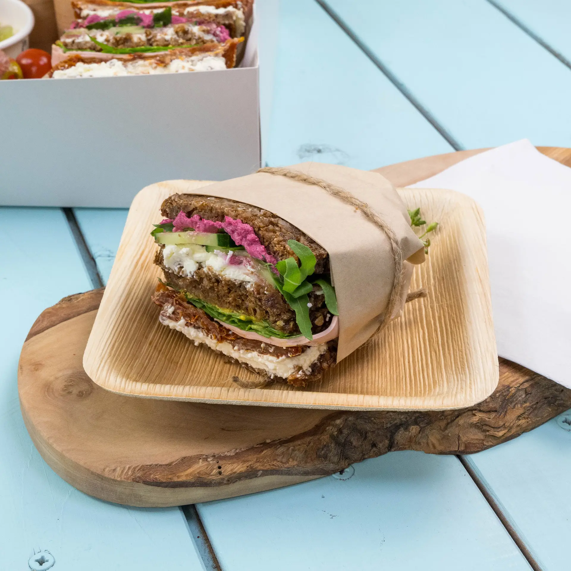 Een ingepakt sandwich met groene rucola, roze smeersel en lagen groenten, presenteerd op een houten bord.