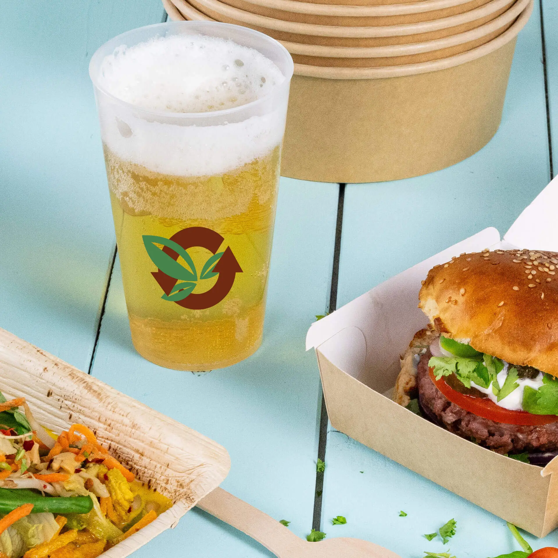 Herbruikbare 400 ml beker met logo en schuimbier, naast een burger en salade op een blauwe houten tafel.