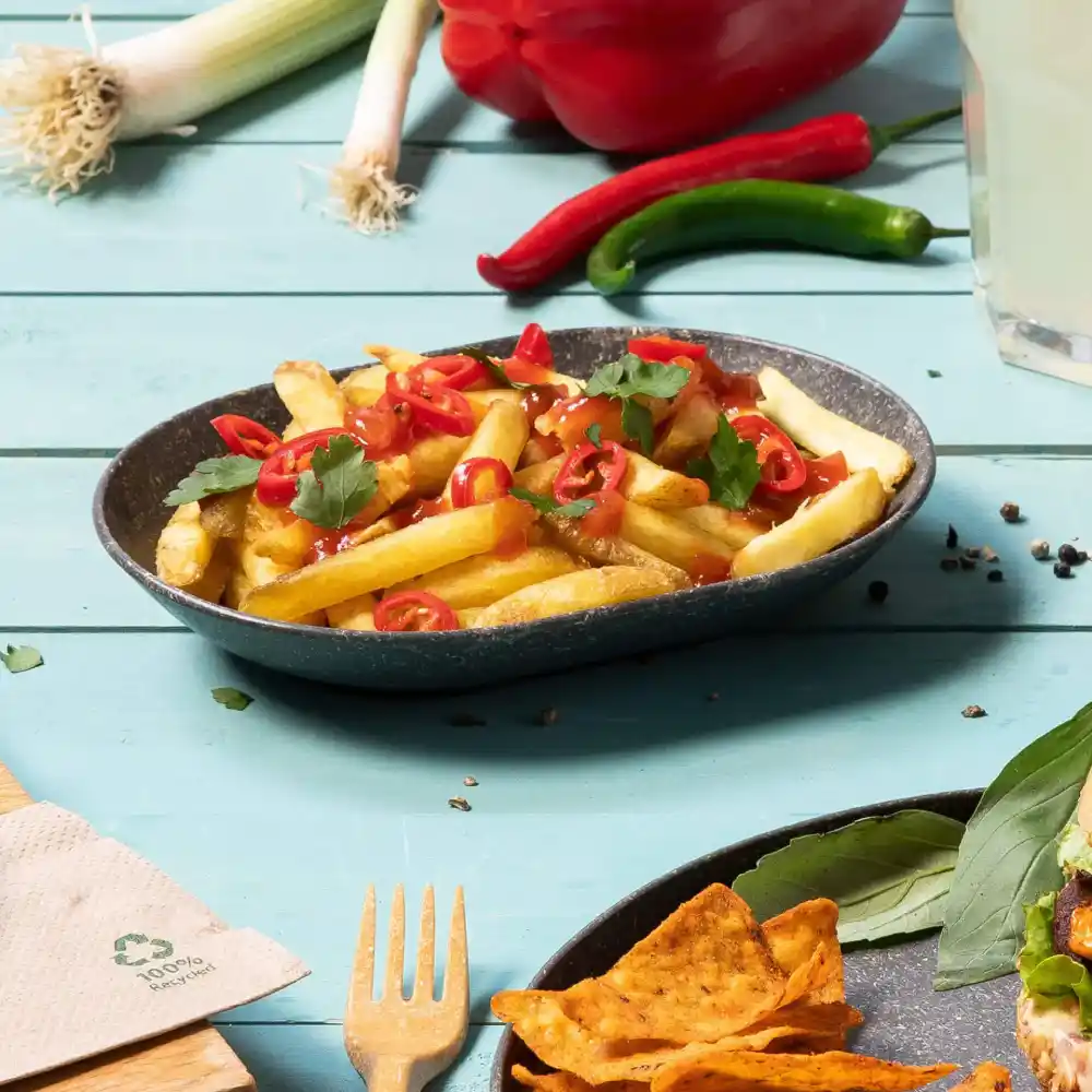 Kom met frietjes, gegarneerd met in plakjes gesneden chili en koriander op een blauwe houten tafel.