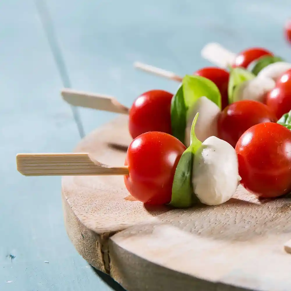 Spiesjes met cherrytomaten, basilic en mozzarella-balletjes op een houten serveerplank.